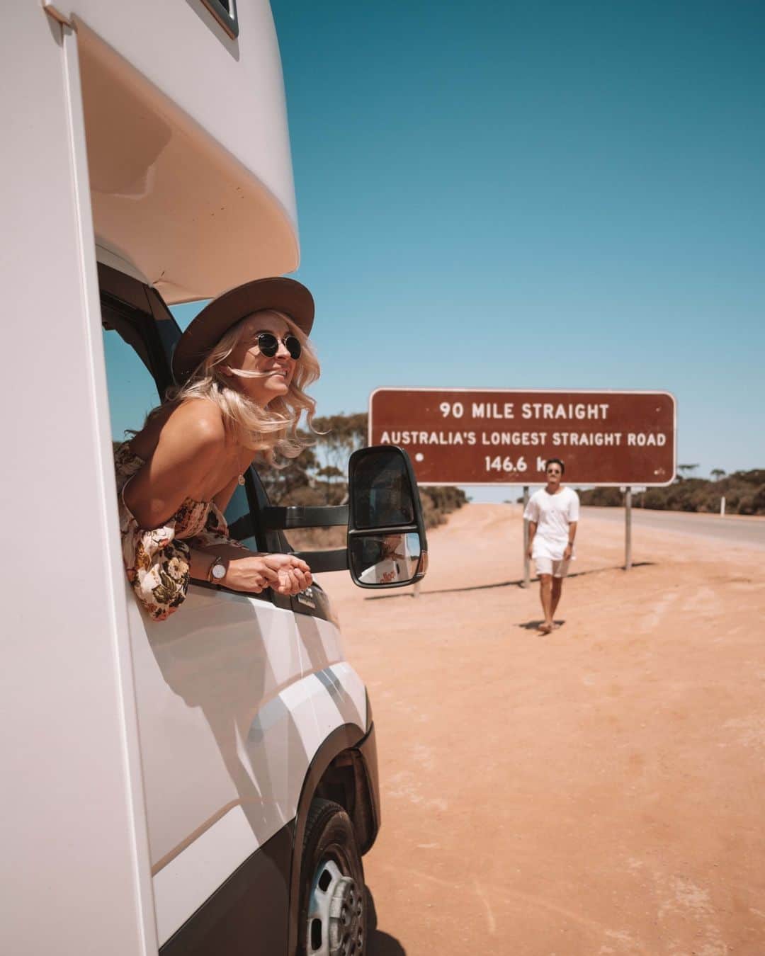 Australiaのインスタグラム：「The epic #Aussie outback needs no introduction 🙌 When it comes to road trip adventures, the #EyreHighway is up there with the best of them. Crossing the #NullarborPlain between Norseman in @westernaustralia and Caiguna in @southaustralia is an iconic journey; where you're sure to uncover interesting people and places along the way 🚙. You'll travel both the dramatic coastline of @eyrepeninsula and the rugged plains of @australiasgoldenoutback, and calling into the famous @nullarborroadhouse is a must.  #SeeAustralia #ComeAndSayGday #WATheDreamState #GoldenOutback  ID: A woman leans out of a car window wearing a hat and sunglasses while smiling, as a man walks across a sandy landscape with a brown sign behind him reading ‘90 Mile Straight, Australia’s longest straight road, 146.6km'」