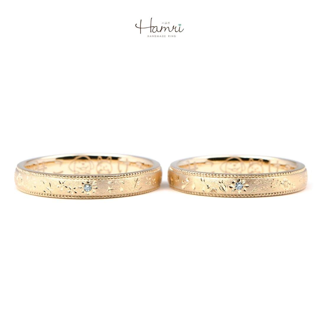 結婚指輪・婚約指輪『Hamri(ハムリ)』のインスタグラム：「【お花彫りデザインの指輪をご紹介です】  この指輪は、KentaさんとMisakiさんの愛の物語を優しい花々で綴るようなデザインです。  指輪に施されたお花畑の彫りは、穏やかな春の日のように、心温まる愛の景色を描いています。  細やかなミルグレインの加工は、指輪にさりげなく華やかな印象をもたらし、  その中で静かに輝くアイスブルーダイヤモンドは、KentaさんとMisakiさんの間の特別な愛を象徴し、永遠の美しさを約束します。  この指輪は、KentaさんとMisakiさんの手元で優しく時を刻み、二人が共に過ごす毎日を、愛とともに穏やかに彩ります。  まるで永遠の愛のように、変わらぬ美しさを保ち続けるでしょう。  内側にはなんと、お二人が自分たちで手書きした超キュートなペットのイラストが入っているんです！  この手書きイラストは、お二人のペットへの愛情がたっぷり詰まった、世界で1つだけの特別なイラストです！  ご結婚おめでとうございます！  💓ふたりらしい指輪と想い出を💓 @hamri_omotesando ==========================  ♦︎♢作成中の写真や動画を撮影、全データプレゼント♢♦︎  DMやLINEでのご相談お待ちしております♥ ⇒@hamri_omotesando  ❁・❁・❁・❁・❁・❁・❁・❁・❁・❁・❁  ＊セットリング5%OFF＊  @hamri_omotesando  Hamri「ハムリ」  〒150-0001 東京都渋谷区神宮前5-11-11 2F  tel 0120-121-175 hp https://hamri.jp/  open 11:00〜19:00 close 火/水　祝日営業  ❁・❁・❁・❁・❁・❁・❁・❁・❁・❁・❁  #手作り結婚指輪 #手作り婚約指輪 #結婚指輪#マリッジリング #エンゲージリング #プレ花嫁 #Hamri #Hamri表参道 #オーダーメイドリング #鋳造 #ブライダルリング #ペアリング #鎚目リング #プラチナリング #ピンクゴールド #シャンパンゴールド #ゴールドリング #コンビネーションリング #2023wedding #2023春婚 #2023夏婚 #プレ花嫁準備 #プレ花嫁と繋がりたい #結婚指輪探し #結婚指輪選び #結婚準備  《Hamri検索タグ》  #hamriデザイン #hamri指輪作り #hamri花嫁」