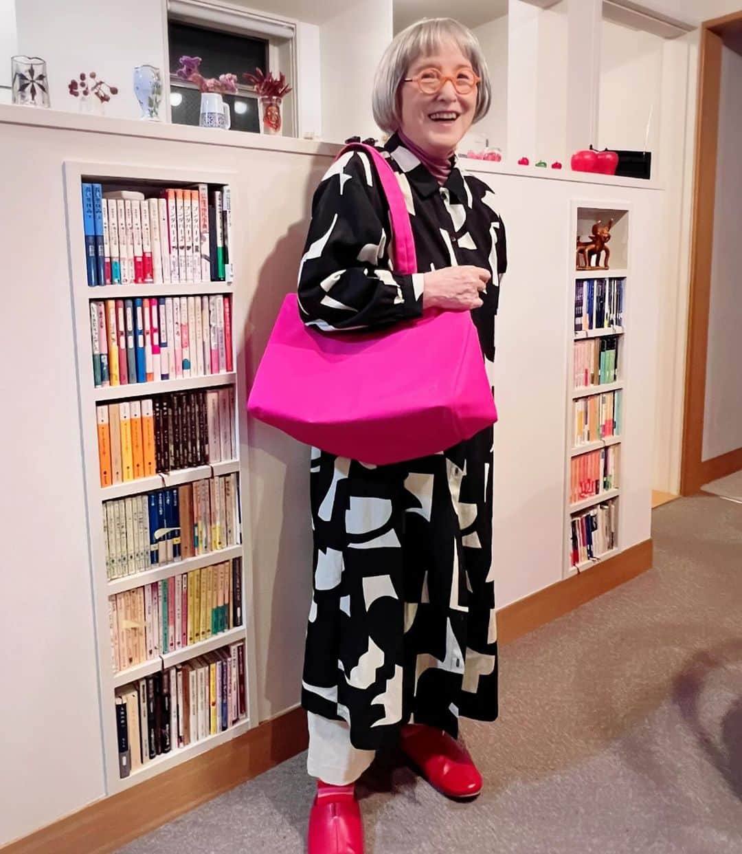 角野栄子のインスタグラム：「私のカラフルワンピースばかり作っていて、少々お疲れ気味の娘りお。 シックな黒白ワンピもたまには作りたい！　それで出来たシャツワンピを着てみました。すると大きな袋を持たされて、これは超カラフルピンク。カバの口みたいにガバッと開く、レジカゴバック。 ワンピもバッグも文学館のショップで売っているんですって。 宣伝みたいになっちゃうから私はいやだ！って言ったのだけど・・・。 リオを筆頭にグッズ制作スタッフたちにお願いされてしまいました。インスタに載せちゃいました。すいません。 黒白ワンピは、案外気にいっています。 ピンクのバッグを持って買い物に行ったら、「あれ、角野さん？」なんて、声かけられちゃった。ふふふ  @eiko.kadono   #魔法の文学館 #いちご色 #ワンピース #カラフルな魔女の物語 #ショッピングバッグ #レジカゴバッグ   My daughter made only my colorful dresses and she is a little tired.  She would like to make a chic black and white dress for a change.  So, I tried her finished shirt dress on. Then I was given a big bag, which is extra-colorful pink.  It’s a shopping-basket-like bag that opens wildly like a hippo’s mouth.   I heard that both this dress and the big bag are sold at the Kiki’s Museum of Literature shop.  Even though I’m not willing to say, because it’s  like an advertising…, but my Rio and the goods production staffs requested to introduce.  So, I put it on my Instagram.  Excuse us! Unexpectedly I liked my this black and white dress.  And then I went shopping with this pink bag, a stranger spoke to me, "Oh, aren’t you Kadono-san?" Tee-hee...」