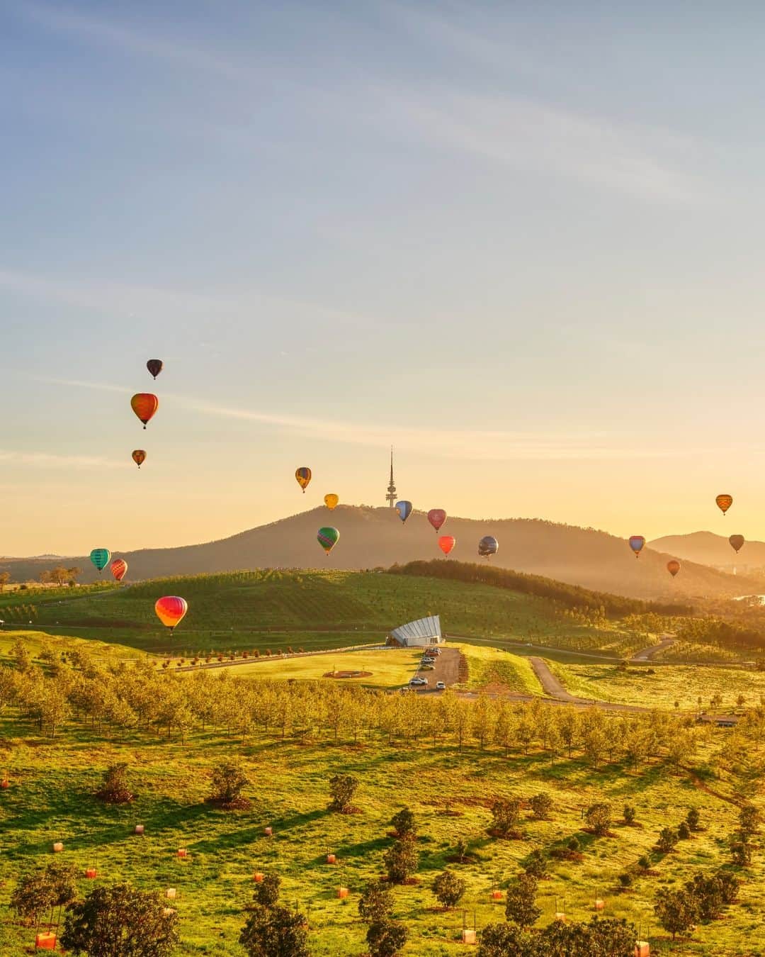 Australiaのインスタグラム：「Early bird gets the views on Ngunnawal Country 🍃🤩 #Australia's capital, @visitcanberra, is the perfect location for a city break - boasting a thriving cultural hub, delicious dining scene, and some of the best museums and galleries in the country! We suggest adding a hot air balloon flight with @balloonaloftcanberra to your itinerary to soak in dazzling views like this☝️Hot tip: visit in March to witness the #CanberraBalloonSpectacular, when dozens of hot air balloons take to the skies above #LakeBurleyGriffin, it's quite the sight to see!   #SeeAustralia #ComeAndSayGday #VisitCanberra #WeAreCBR  ID: multiple hot air balloons rise towards the sky at first light. Green rolling fields are laid out below them. In the distance, a tower can be seen on top of a hill.」