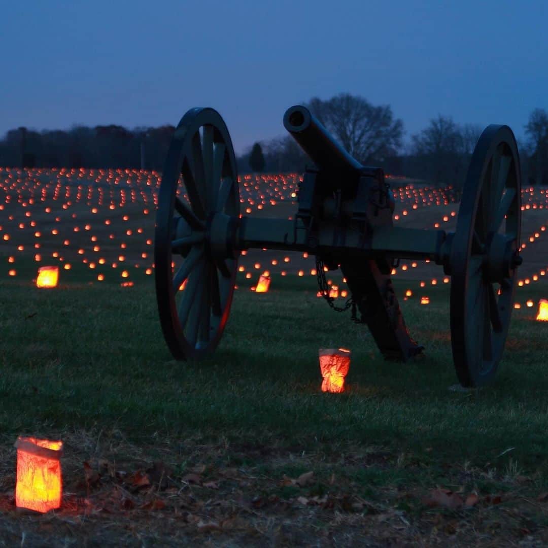 アメリカ内務省のインスタグラム：「Tomorrow (Saturday) evening at @anti1862nps in Maryland, over 23,000 luminaries will light the battlefield — each luminary representing a casualty from the Battle of Antietam.    The hallowed grounds evoke a powerful sense of place, allowing visitors to connect personally to the battle and its participants. The event is a driving tour open to the public starting at 6:00 pm.   Photos by NPS    #publiclands #Antietam   Alt Text:    Photo 1: A Civil War cannon sits in a field with lots of luminaries shining in the distance.    Photo 2: Luminaries are aligned along Bloody Lane during Antietam Battlefield’s Memorial Illumination.」