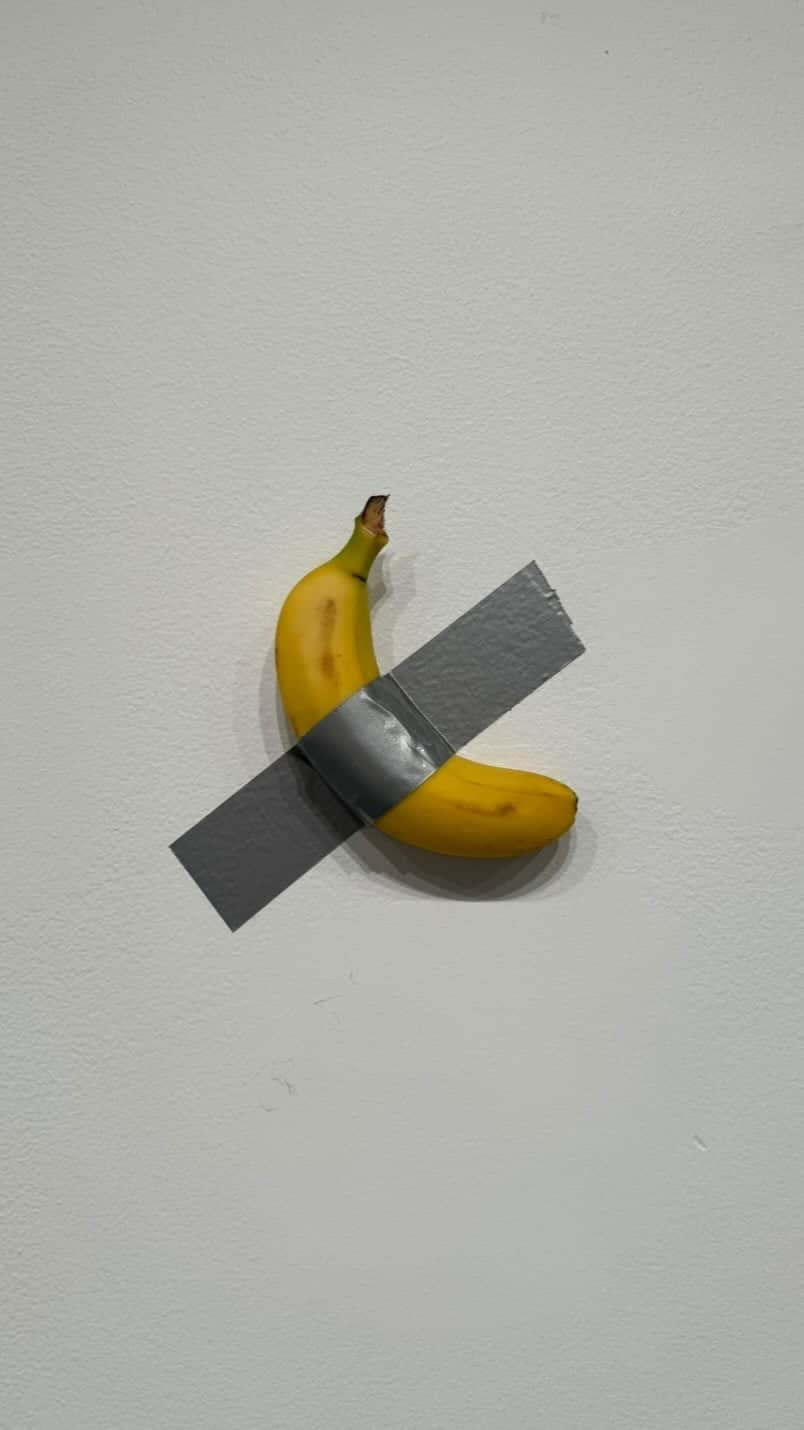 StreetArtGlobeのインスタグラム：「Is this art or food or something else? 🎨🍌🤷🏽‍♂️  The National Gallery of Victoria exhibits a banana sculpture as part of its Triennial exhibition.   The work is titled “The Comedian” and is by Italian artist Maurizio Cattelan. Another edition of this work has previously sold for $120,000 USD.   The work has courted a lot of controversy in the past, not just because it is ‘simply’ a banana duct taped to the wall, but because some hungry passers-by have decided to eat it as a snack.   When it was originally exhibited at Art Basel Miami in 2019, performance artist David Datuna yanked it off the wall and ate it as part of his own performance called “Hungry Artist”.   When the work was exhibited again in Seoul, South Korea in April 2023, student Noh Huyn-soo removed the banana from the wall and started eating it, claiming he “was hungry”. When he was finished, he taped the banana skin back to the wall.   What do you think about this work? Apeeling or not? 🤷🏽‍♂️🍌  Featuring @ngvmelbourne / @mauriziocattelan / @katprugger / @david_datuna / @artbasel」