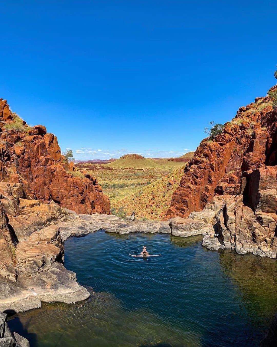 Australiaのインスタグラム：「@australiasnorthwest is a pretty great spot to put your feet up if you ask us 🤷 Within #MillstreamChichesterNationalPark, on the lands of the Yinjibarndi people, you'll find stunning spots like #PythonPool, where rugged red rocks frame beautifully untamed landscapes 💚 Starting from #Karratha in the #Pilbara region, step into the wilds of this epic part of @westernaustralia on a 4WD camping adventure with @ngurrangga_tours 🚙🏕️ Explore ancient rock art, forage for bush foods and hear local stories as you tag along with Traditional Custodians (📸: @travellinwa).   #SeeAustralia #ComeAndSayGday #WATheDreamState #AustraliasNorthWest  ID: A person floating on their back in a tranquil pool surrounded by red, rocky cliffs while overlooking a rugged green expanse on a sunny day.」