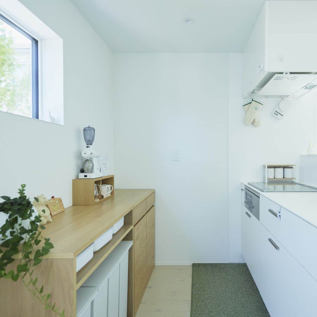 無印良品の家さんのインスタグラム写真 - (無印良品の家Instagram)「【住まいの実例】 ※右上のブックマークのアイコンをタップすると保存できます。  ご住所：神奈川県茅ケ崎市 竣工年月：2022年5月 延床面積：110.13m²  神奈川県茅ケ崎市に建つ「窓の家」S邸。真っ白い壁と三角屋根が個性的なお宅ですが、住宅地にも溶け込むシンプルさとナチュラルさも兼ね備えています。ご家族はこの家に住んで1年半が経ちました。  もともとは都心に程近い賃貸マンションに住んでいたご家族。ご主人がリモートワーク中心の働き方となり手狭になったことから郊外でゆったりと暮らせる戸建ての家づくりが始まりました。  当初から考えていた間取りのこだわりはご主人のリモートワークをするための仕事部屋とお子さまの子ども部屋です。この二つは個室にする予定でしたが、担当者からの提案を何度か変更して仕事部屋は寝室内に収めました。この結果スペースが少し増えたことで、フリースペースも広めに取ることができました。  キッチンは奥さまの希望を反映させて、実用面での快適さとみせる・隠すを意識した美しいデザインに。  「私の身長が少し高いのでキッチンも高めに設計してもらいました。腰を曲げずに料理ができるのでとても楽です。キッチンカウンターも高めにしています。ダイニング側から見たときに水回りが見えないのでスッキリ見えますし、料理ができたときに家族に運んでもらう配膳台としても機能しています。リビング全体を見渡せるので子どもがリビングで宿題やゲームをしていてもコミュニケーションが取れるのがいいですね」（奥さま）  冷蔵庫スペースの隣にはパントリーを作って収納力も抜群。またキッチン奥には背の低い食器棚を置くことで見せたいものだけ見せて見せたくないものをしっかり隠す、スッキリとした空間を実現しています。  「家の中に風や光を通す“抜け”をなかなか作りにくいのが住宅街に家を建てる難点だと思います。でもこの家なら吹き抜けの大きな窓から空を切り取って眺められます。ソファに座って窓を見上げると雲の流れや月、飛行機を見ることができるのはとても贅沢ですね。リビングの大きな室内窓から部屋中に光も入ってきて外が暗くなるまでずっと家の中が明るいのも気持ちがいい。日常の中に非日常やちょっとした浮遊感を味わえるのはこの家だからこそだと思います」（ご主人）  2023.12.5公開住まいの実例『窓から光、空、緑を取り込み、暮らしのある美術館のような家へ』より  詳しくはプロフィールハイライトか、「無印良品の家」HPをご覧ください。  @mujihouse」12月6日 17時00分 - mujihouse