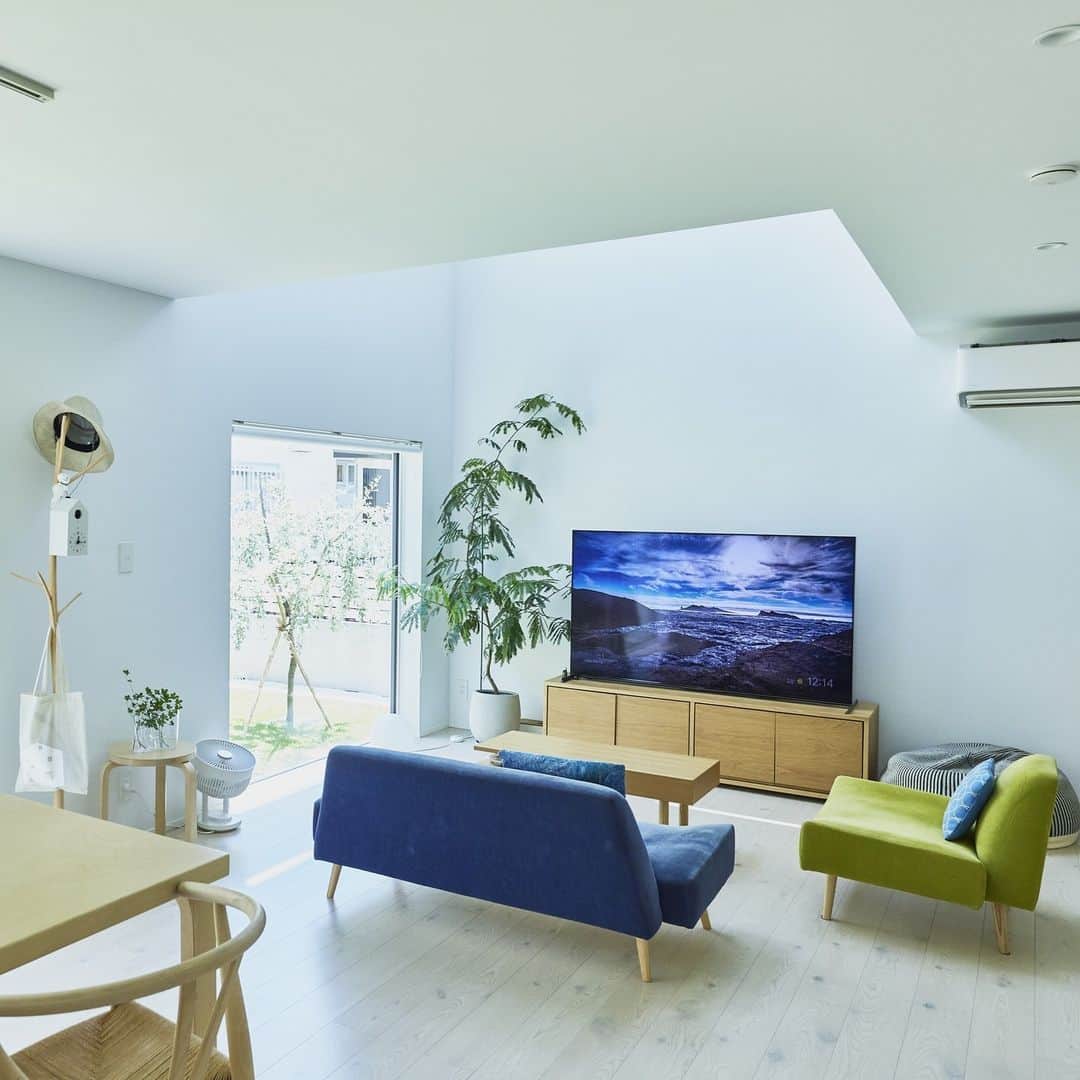 無印良品の家のインスタグラム：「【住まいの実例】 ※右上のブックマークのアイコンをタップすると保存できます。  ご住所：神奈川県茅ケ崎市 竣工年月：2022年5月 延床面積：110.13m²  神奈川県茅ケ崎市に建つ「窓の家」S邸。真っ白い壁と三角屋根が個性的なお宅ですが、住宅地にも溶け込むシンプルさとナチュラルさも兼ね備えています。ご家族はこの家に住んで1年半が経ちました。  もともとは都心に程近い賃貸マンションに住んでいたご家族。ご主人がリモートワーク中心の働き方となり手狭になったことから郊外でゆったりと暮らせる戸建ての家づくりが始まりました。  当初から考えていた間取りのこだわりはご主人のリモートワークをするための仕事部屋とお子さまの子ども部屋です。この二つは個室にする予定でしたが、担当者からの提案を何度か変更して仕事部屋は寝室内に収めました。この結果スペースが少し増えたことで、フリースペースも広めに取ることができました。  キッチンは奥さまの希望を反映させて、実用面での快適さとみせる・隠すを意識した美しいデザインに。  「私の身長が少し高いのでキッチンも高めに設計してもらいました。腰を曲げずに料理ができるのでとても楽です。キッチンカウンターも高めにしています。ダイニング側から見たときに水回りが見えないのでスッキリ見えますし、料理ができたときに家族に運んでもらう配膳台としても機能しています。リビング全体を見渡せるので子どもがリビングで宿題やゲームをしていてもコミュニケーションが取れるのがいいですね」（奥さま）  冷蔵庫スペースの隣にはパントリーを作って収納力も抜群。またキッチン奥には背の低い食器棚を置くことで見せたいものだけ見せて見せたくないものをしっかり隠す、スッキリとした空間を実現しています。  「家の中に風や光を通す“抜け”をなかなか作りにくいのが住宅街に家を建てる難点だと思います。でもこの家なら吹き抜けの大きな窓から空を切り取って眺められます。ソファに座って窓を見上げると雲の流れや月、飛行機を見ることができるのはとても贅沢ですね。リビングの大きな室内窓から部屋中に光も入ってきて外が暗くなるまでずっと家の中が明るいのも気持ちがいい。日常の中に非日常やちょっとした浮遊感を味わえるのはこの家だからこそだと思います」（ご主人）  2023.12.5公開住まいの実例『窓から光、空、緑を取り込み、暮らしのある美術館のような家へ』より  詳しくはプロフィールハイライトか、「無印良品の家」HPをご覧ください。  @mujihouse」