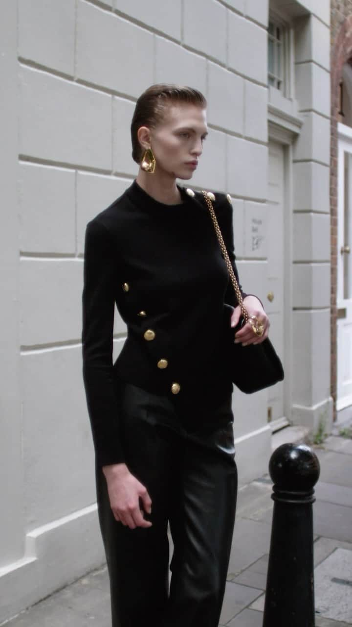 アレキサンダー・マックイーンのインスタグラム：「A black asymmetric knit jumper with gold seal buttons and wide-legged trousers worn with a black #McQueenSeal bag and modernist jewellery.  Discover the #McQueenPreSS24 collection via the link in bio.  Video by @EbbaHult⁣⁣⁣ Music Director - John Gosling ⁣⁣ Track - Leipzig by Toby Andersen」