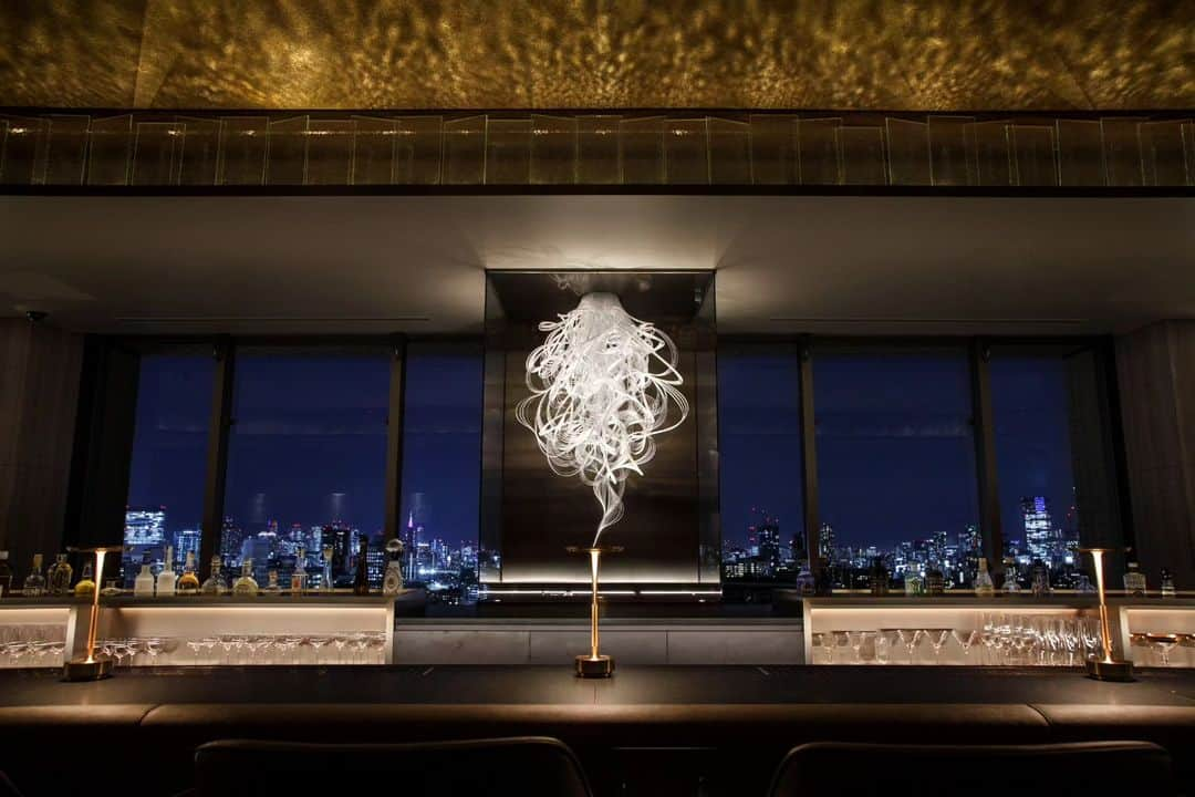 THE WESTIN TOKYO | ウェスティンホテル東京さんのインスタグラム写真 - (THE WESTIN TOKYO | ウェスティンホテル東京Instagram)「ビール工場の煙突から立ちのぼる「煙」をデザインモチーフに“Smoke/Reflection/Surprise”というコンセプトのもと、幻想的な光が演出するスカイバー「エスカリエ」がグランドオープしました✨  最上階までたどり着いたゲストだけが、東京眺望とここだけにしかないカクテルとデザートを味わえる、そんなサプライズのある場所という意味を込めてフランス語の「階段＝エスカリエ」と名づけました。  シークレットドアを開ければプロンズを基調とした内装と東京の眺望が目の前に広がり、最上階からの心躍る驚きをご堪能いただけます。また、フロア窓際のソファーシートでは、東京の美しい夜景を眺めながらプライペート感あふれる時間をお過ごしいただけます。  世界中から集められたプレミアムスピリッツも数多くご用意。ミクソロジーの技術を駆使した季節のカクテルに加え、ワールドトップバーテンダー後閑信吾氏率いる世界最高のバーアワード「THE WORLD'S 50 BEST BARS」に輝く「The SG Club」がエスカリエのために創作した7種類のカクテル・ノンアルコールカクテルも揃えました。総料理長沼尻寿夫による大人のデザートもお楽しみいただけます。     詳細はプロフィールのリンクより🔗  Based on the concept of “Smoke, Reflection & Surprise”, the sky bar “Escalier” has opened its doors, along with an elegant and refined selection of cocktails✨  Only the guests who reach the top floor of The Westin Tokyo can enjoy the beautiful views and the cocktails and desserts exclusive to this bar, named after the French word for “Staircase”.  Open the secret door to this haven and reveal all of its surprises, from the bronze based interior design, to the sofa seats next to the windows where you can enjoy a private time while admiring the breathtaking night view of Tokyo.  "Escalier" also offers a wide variety of premium spirits from around the world and seasonal cocktails crafted using mixology techniques. To top it off, seven types of cocktails (including non-alcoholic mocktails) created exclusively for “Escalier” by the world-renowned bartender Shingo Gokan are also available alongside desserts created by executive chef Hisao Naganumajiri.  Join us for a night full of surprises and delight at The Westin Tokyo sky bar, "Escalier".  For more details please visit our bio link 🔗  #ウェスティンホテル東京 #ウェスティンホテル #ウェスティン #ホテル #日本 #東京 #改装 #グランドオープン #ホテルグランドオープン #バー #プレミアムスピリッツ #カクテル #後閑信吾 #スカイバー #眺望 #WestinTokyo #westinhotel #Escalier #skybar #cocktails #dessert #grandopening #mixology #skyline #views #mocktails #bronze #SingoGokan #Hisaonaganumajiri」12月7日 18時59分 - westintokyo