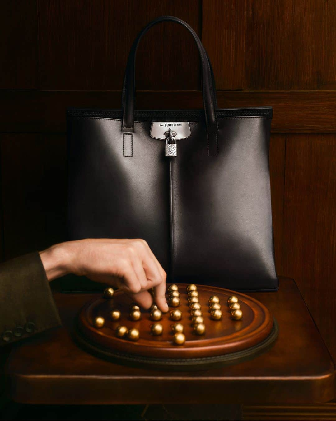 ベルルッティのインスタグラム：「- HOLIDAY SCENES WITH #BERLUTI -   Dare to be extraordinary this holiday season: the utmost embodiment of Berluti’s flair for craftsmanship, Luti 38 is a spacious bag made of Venezia leather, and featuring Norwegian stitching details, a metallic lock-and-padlock closure and a bold Nero Grigio patina. It is the perfect companion for the leather-and-brass material combination of Les Passe-Temps’ game of solitaire.   Now available on the e-shop.   Creative direction by @trendsandculture for Berluti Photo by @jamesharveykelly   #BERLUTIHOLIDAY #BERLUTIGIFT」