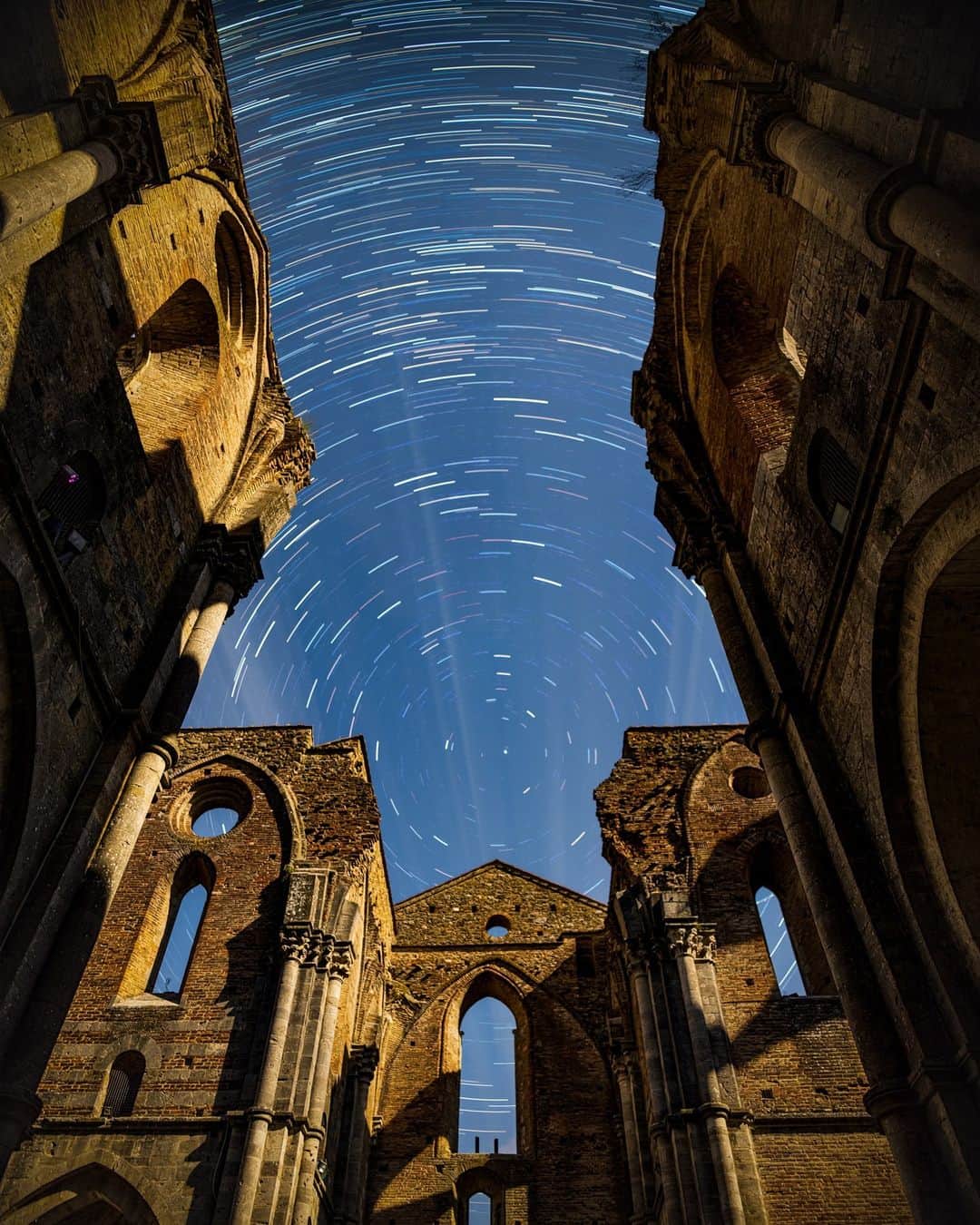 National Geographic Travelのインスタグラム：「Photo by @babaktafreshi | On a moonlit night in Italy, star trails rotate above the roofless Abbey of Saint Galgano near Siena, Tuscany. In the 18th century, the unique 13th-century Gothic-style abbey was hit by a lightning bolt, which caused the bell tower to fall onto the church, destroying the roof. In this long-exposure image, Earth’s rotation causes star trails around the north celestial pole (marked by Polaris).」