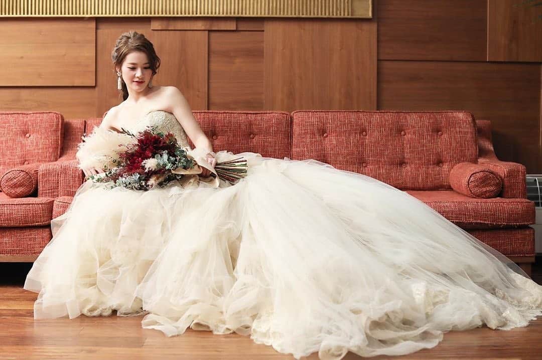 25ans Wedding 公式 Bridesのインスタグラム：「今日もYUKAさんのフォトをリポスト💐 ニュアンスカラーのドレスに、深みのあるレッドを中心にくすみカラーでまとめたブーケがよく馴染みます。稲穂にも似たパンパスグラスの穂先は、ふんわりとボリューミーなスカートのシルエットにベストマッチ☺️」