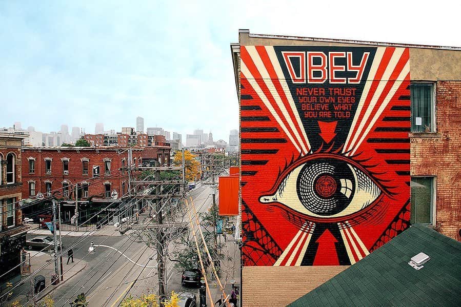 Shepard Faireyのインスタグラム：「Toronto was the last stop on my seven-city mural tour back in 2014. It was a fun place to end the trip, and we had a solid crew from @obeyclothing from Canada and the U.S. to support and rage at various parties and grimy dives. Romeo Trinidad and Jon Furlong were up early to help with installation and photography despite the late nights. My crew, Nic Bowers, Rob Zagula, and Dan Flores, were essential to the deft completion of the two murals we did there - one on a music venue called The Tattoo (where the great Hennessy party went down) and the other on an art-themed hotel called The Gladstone. The proprietors and staff of both venues were incredibly generous hosts. I walked around Toronto’s Queen West district, putting up stickers, and I found a bunch of cool record stores, cafes, bars, boutiques, and more, I loved the area. Beyond just the euphoria of finding a Dead Kennedys 7″ singles box set, I could see hanging out in that area of Toronto for more than just a few days. Toronto’s people were super cool too. I got to hang with some great artists, including Gary Taxali and the Lovebot crew, who were friendly and genuine. There is a lot of good street art and graffiti in parts of Toronto too, so the city gets two thumbs up. As Keith Haring said, “the public has a right to art,” and after many years of hit-and-run street art, and many arrests, I’m working every angle I can to bring free art to the public on a larger scale. I want to thank every person in every city who helped to facilitate these murals. THANK YOU! Once this pandemic settles, there will be a lot more to come! -Shepard 📷: @jonathanfurlong」