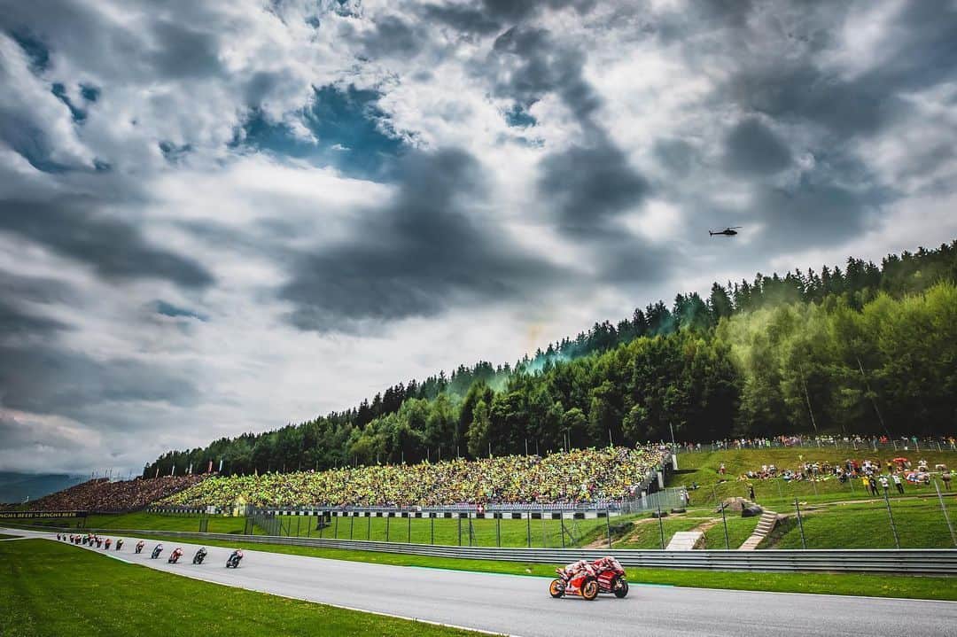 レプソル・ホンダのインスタグラム：「#ThrowbackThursday - Through the Lens - @polarityphoto ⠀⠀⠀⠀⠀⠀⠀⠀⠀ Let battle commence! It only took a few seconds for Marc and Andrea to lock horns at the Red Bull Ring and after just one corner they had set the tone for the rest of the race. I decided to shoot the start from here to capture a wide view of the racing amongst the rolling hills, flare smoke and packed grandstands. I remember feeling like I was waiting for the lights to go out for a long time, and then when they did, within seconds the pack were screaming up the hill and past me in the blink of an eye. ⠀⠀⠀⠀⠀⠀⠀⠀⠀ 1/2000 sec. f/7.1 16 mm ISO 100」