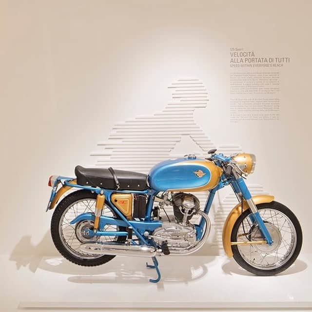 のインスタグラム：「Ducati Heritage/125スポーツ  まさにレーサーレプリカマシン。それがベベルギア駆動の単気筒エンジンを積む「125スポーツ」です。 1950年代に、ヨーロッパの街と街の間で争われた都市間レースなどで圧倒的速さを見せつけたレーシングマシン「Gran Sport ’マリアンナ’」の公道バージョンとして開発。現在ドゥカティの各モデルはベルト使ってシリンダーヘッドに収めたカムシャフトを駆動していますが、ベベルギア駆動のエンジンは、円すいの両端にかさ歯車が付くベベルギアを介したバルブ駆動システムを採用していました。静粛性が高く、コンパクトで高い強度を持っているのが特徴。シリンダー中央に配置した円柱状のベベル・カバーがドゥカティのアイコンにもなりました。  125スポーツの物語はプロフィール( @ducatijapan )のリンクよりHeritage - The Ducati historyの「1946-1960」からご覧ください。  #ドゥカティいいじゃん #DucatiHeritage #バイク #バイクのある生活 #バイクのある風景 #motorcycle #bike #ツーリング」