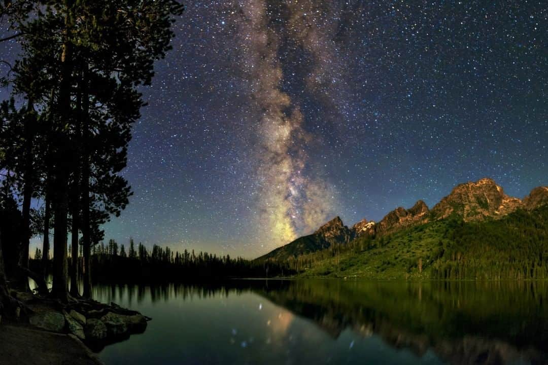 National Geographic Travelさんのインスタグラム写真 - (National Geographic TravelInstagram)「Photo by @babaktafreshi  From Earth to the Universe  The night sky glows above a lake in Grand Teton National Park in Wyoming. The bright summer Milky Way stands above the Teton Range, lit by the rising moon on the opposite horizon. There are not many places left on the planet to enjoy the natural starry sky. Most of humanity experiences light-polluted night skies and to many the Milky Way is no longer visible, but dark sky protected places like this save this essential part of our environment.  Search for “World’s Best Stargazing Sites” on natgeo.com for an article on my top 10 dark sky locations, based on two decades of night sky photography around the world. Learn more @babaktafreshi and @idadarksky. #twanight #grandteton #stargazing #nationalparks」7月10日 13時09分 - natgeotravel