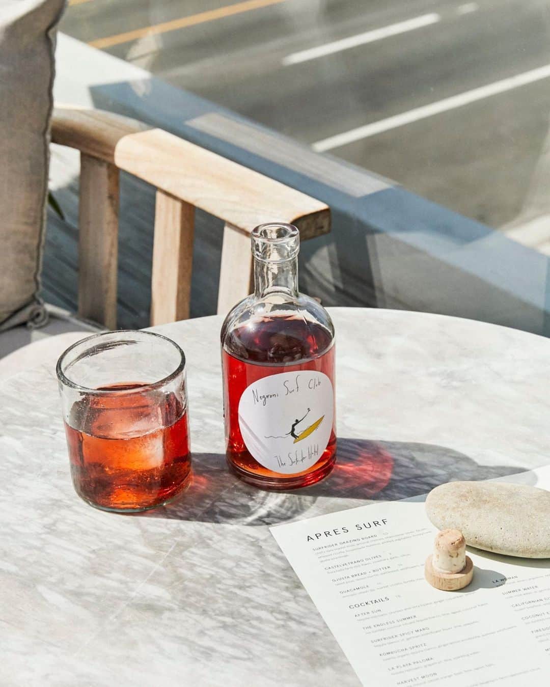 MR PORTERのインスタグラム：「For tonight's cocktail hour we are joining Mr Matt Goodwin on the deck of his hotel @thesurfridermalibu for a spot of Apres Surf. The hotel isn't a stranger to a party and is situated next door to the Crazy Horse Saloon (which was, at one point, owned by Mr Neil Young) and legend has it that Young, Hendrix, The Doors and Mr Bob Dylan use to play their shows and then party at The Surfrider afterwards.   The team have channelled that carefree spirit into their cocktails and on the menu this evening is a Negroni Surf Club. Mix it up with the instructions below (or if you are lucky enough to be local you can pop by and pick one up pre-bottled for your next beach picnic)   Negroni Surf Club  1oz Amass Gin 1oz Campari 1oz Punt e Mes  Pour ingredients into a glass cocktail mixer, with three cubes of ice, gently stir in a circular pattern for 30 seconds. Prepare 12oz rocks glass with a large single cube of ice, strain and pour negroni mix onto cube of ice in glass. Add freshly peeled orange or bergamot rind for a garnish. Stir around the glass one time for scent 🍊  #MRPORTERGoneSurfin 🏄‍♂️ Bottle designed by @thecartorialist 📷@trevorkingphoto」