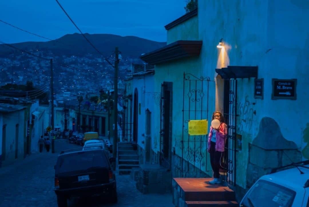 National Geographic Travelさんのインスタグラム写真 - (National Geographic TravelInstagram)「Photo by @francescolastrucci  The night before Dia de Los Muertos, a girl inflates a balloon in front of her house in Oaxaca de Juarez, Mexico. The Day of the Dead, of pre-Hispanic origin and dedicated to loved departed souls, is one of the most important celebrations in the country. The celebration is particularly significant in Oaxaca, where Catholic rituals are mixed with the pre-Colombian elements so strong in the region. I particularly loved photographing during twilight on this occasion, where I was looking for images that could represent the mysticism hovering in the air. Climbing on one of the densely inhabited hills surrounding the historic center of the city looking for a wider view, I found myself waiting for almost half an hour in front of an illuminated door, beyond which I heard voices coming. Finally and to my surprise, the girl with the balloon gave me the moment of serendipity and magic that I was looking for. Follow me @francescolastrucci for more places, daily life, and stories around the world. #oaxaca #mexico #dailylife」7月28日 17時09分 - natgeotravel