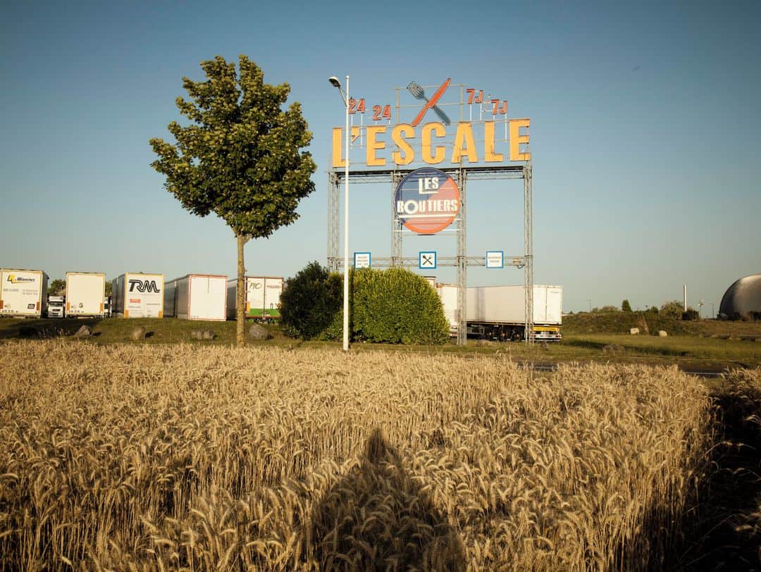 ルモンドさんのインスタグラム写真 - (ルモンドInstagram)「« L’Escale 24 24, 7J/7J. » Visible depuis l’autoroute A 20, ce monumental écriteau lumineux, agrémenté d’une fourchette bleue et d’un couteau rouge croisant le fer, clignote au fond d’un champ qui réclame sa moisson. Ici, à Déols (Indre), et tout le temps, les routiers sont chez eux. Passés le portique, les voilà qui s’étalent sur un vaste parking, sans un regard pour les Courtepaille, Buffalo Grill et autre Pataterie alignés non loin. La journée s’achève, et quarante camions ont déjà pris place. La plupart sont immatriculés en France, en Estonie et au Portugal. Parmi eux, deux beaux 44-tonnes blanc et bleu, disposés côte à côte.⁣ Ceux d’Audrey, 28 ans, recrutée par son transporteur il y a deux semaines, et d’Alain, 63 ans, routier retraité qui rempile pour un contrat de quatre mois. « C’est un secteur en tension et j’avais une toiture à refaire. Cela va payer les ardoises. » Pour le compte d’une enseigne de la grande distribution, les deux ont transporté du poisson depuis la criée de Lorient (Morbihan) jusqu’à un entrepôt de Bourges. Un nouveau chargement, dont ils ignorent le contenu, les attend demain après-midi, à Tours.⁣ L' Escale, le plus grand restaurant routier de France, a rouvert ses portes, début juin, après trois mois de fermeture pendant le confinement. Mais les clients tardent à revenir.⁣ -⁣ 1 : Les semaines passent, la reprise n’est pas au rendez-vous. Les chauffeurs routiers sont fidèles, mais la clientèle des discothèques et des spectacles a disparu.⁣ 2 : En cuisine ainsi que dans les salles, le masque anti-Covid est imposé au personnel et à la clientèle.⁣ 3 : L' Escale, le 9 juillet.⁣ 4 : Les routiers sont ici chez eux et peuvent profiter de douches à l’italienne.⁣ -⁣ Photos : Claude Pauquet (@claude.pauquet) / VU ( @vu_photo) #PourLeMonde⁣ #Routiers #Covid19」7月29日 21時01分 - lemondefr