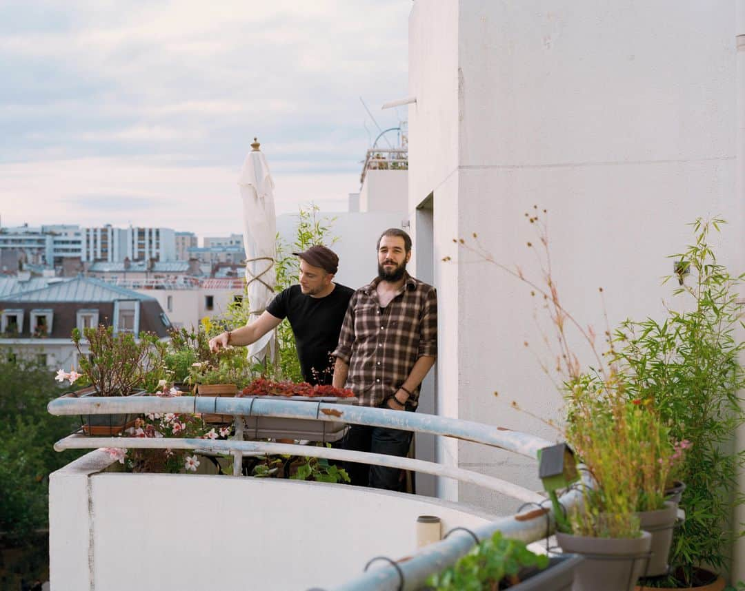 ルモンドさんのインスタグラム写真 - (ルモンドInstagram)「En découvrant le balcon d’Alain Frangeul, on peut être pris d’une hésitation quant au qualificatif approprié. Voici ce qu’il n’est pas : haussmannien, rectangulaire, en fer forgé. Alors… Arrondi ? Un peu. Tortueux ? Peut-être. « En S », corrige Gabriel Frangeul, son fils. « En serpent », complète le père.⁣ Voici ce qu’il est, sans l’ombre d’un doute, ce balcon : la vedette de l’appartement. La raison pour laquelle aujourd’hui trois hommes vivent ici, un père, son fils et le compagnon de celui-ci. Il y a trente-deux ans, Alain Frangeul, habitant du 20e arrondissement parisien, est au chômage, entre deux boulots. Il a travaillé dans les imprimeries maoïstes du coin. Il se promène sur les hauteurs de Belleville, d’où il contemple un vaste chantier. Plus qu’un chantier, une révolution. La disparition pure et simple d’un quartier, et la naissance d’un autre, le nouveau Belleville, avec ses grands ensembles, ses nouvelles rues dont le tracé et le nom sont les seuls rappels du Paris d’antan : rues du Pressoir, Julien-Lacroix, Vilin…⁣ Rue Vilin, justement : depuis son promontoire, Alain Frangeul regarde ce qui se passe ici, dans cette voie photographiée par Willy Ronis. C’est là qu’Alain Frangeul voit un immeuble en train d’être bâti. Il est blanc, en forme de D. « Je suis allé regarder, j’ai vu sur les panneaux que c’était du 1 % patronal, auquel j’étais éligible grâce à mon employeur, et j’ai dit : c’est là que je veux habiter. Comme j’ai fait du forcing, j’ai été parmi les premiers à visiter et on m’a fait choisir l’appartement que je préférais. J’ai pris celui-ci parce qu’il avait ce balcon en serpent. »⁣ -⁣ Gabriel Frangeul (à droite) et son compagnon Alexandre Lenoir sur leur balcon, cité de Gênes, à Paris, le 14 juillet. Photo : Christophe Coënon (@christophecoenon) / SO Represent (@so_represent) #PourLeMonde」8月1日 19時31分 - lemondefr