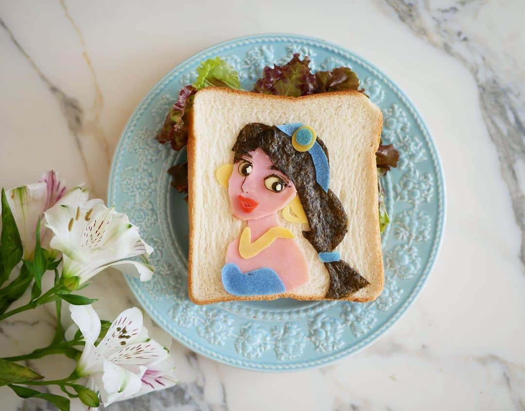 倉岡生夏のインスタグラム：「ジャスミン　サンドウィッチ🥪 ・ ・ ジャスミン気分になって作りました💓 ・ 顔、身体、ハム 髪の毛、のり 目、チーズ 口、赤ウインナー カラー部分、ととしーと ・ ・ ・ プリンセスどんどん作っていきたいなぁ💓 ・ ・ 最近暑いですね💦 朝はフルーツ、手作りジンジャエールで暑さのりきってます⭐️ ジンジャエールレシピ載せますね💓 ・ ・ ・ #おうち時間  #おうちカフェ #ジャスミン  #トーストアート  #愛され料理 #クッキングラム #ディズニートーストアート #ディズニーごはん  #キャラパン  #delistagrammer  #disneygram  #kyaraben  #disneyprincess」