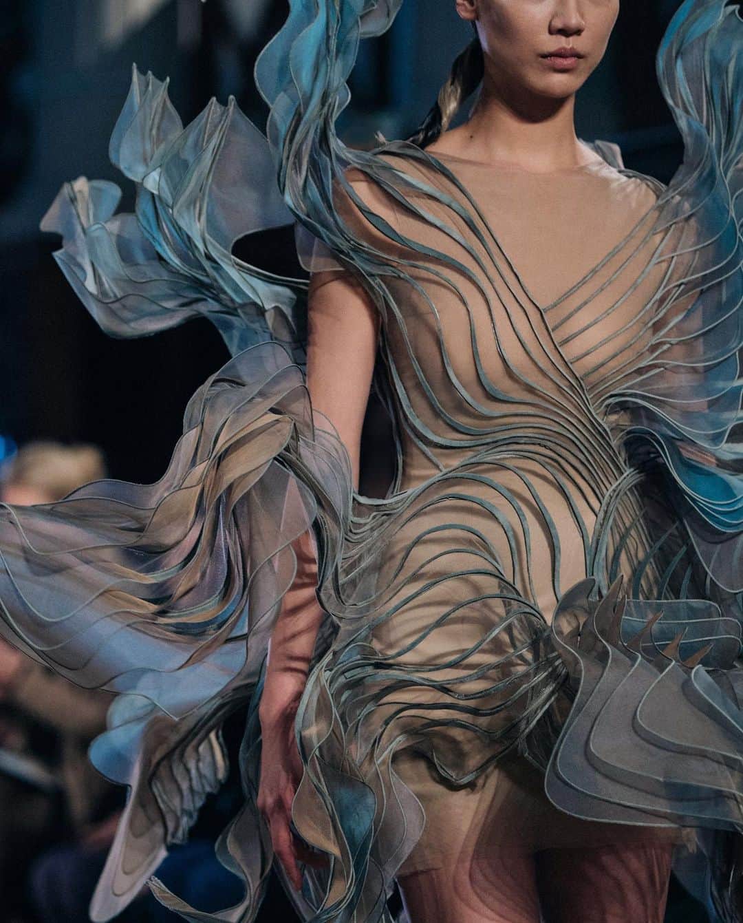 Iris Van Herpeさんのインスタグラム写真 - (Iris Van HerpeInstagram)「‘Craftolution’ Submerge in the intricate details through time, where craftsmanship and innovation intertwine ~  Look 1: Shift Souls Transparent organza is gradient-dyed in sky-blue aqua-patterns that are 3D modelled in CAD software, to then be sliced up and multi-layered into hundreds of fine hand-cut waves, each individually stitched onto a stretch tulle, creating a quivering sculptural silhouette. Look 2: Ludi Naturae A silk changeant organza, mylar and velvet are heat-bonded, lasercut and wire-bonded, creating a voluminous slow motion splash. Look 3: Aeriform A changeant silver lace is lasercut into thousands of thin stretchy lines that are hand-stitched into 3D wave~patterns. Look 4: Mummification Beige toned leather is handcut into fine strings to then be laced into hundreds of metal eyelets, creating an adjustable fit for a transformable corset-dress. Look 5: Shift Souls Vermillion red cloud-printed silk is bonded to mylar and lasercut into the finest lace of thousands of 0.5mm harmonica-waves, creating quivering echos.  #irisvanherpen #couture #detail #archive」8月7日 1時26分 - irisvanherpen