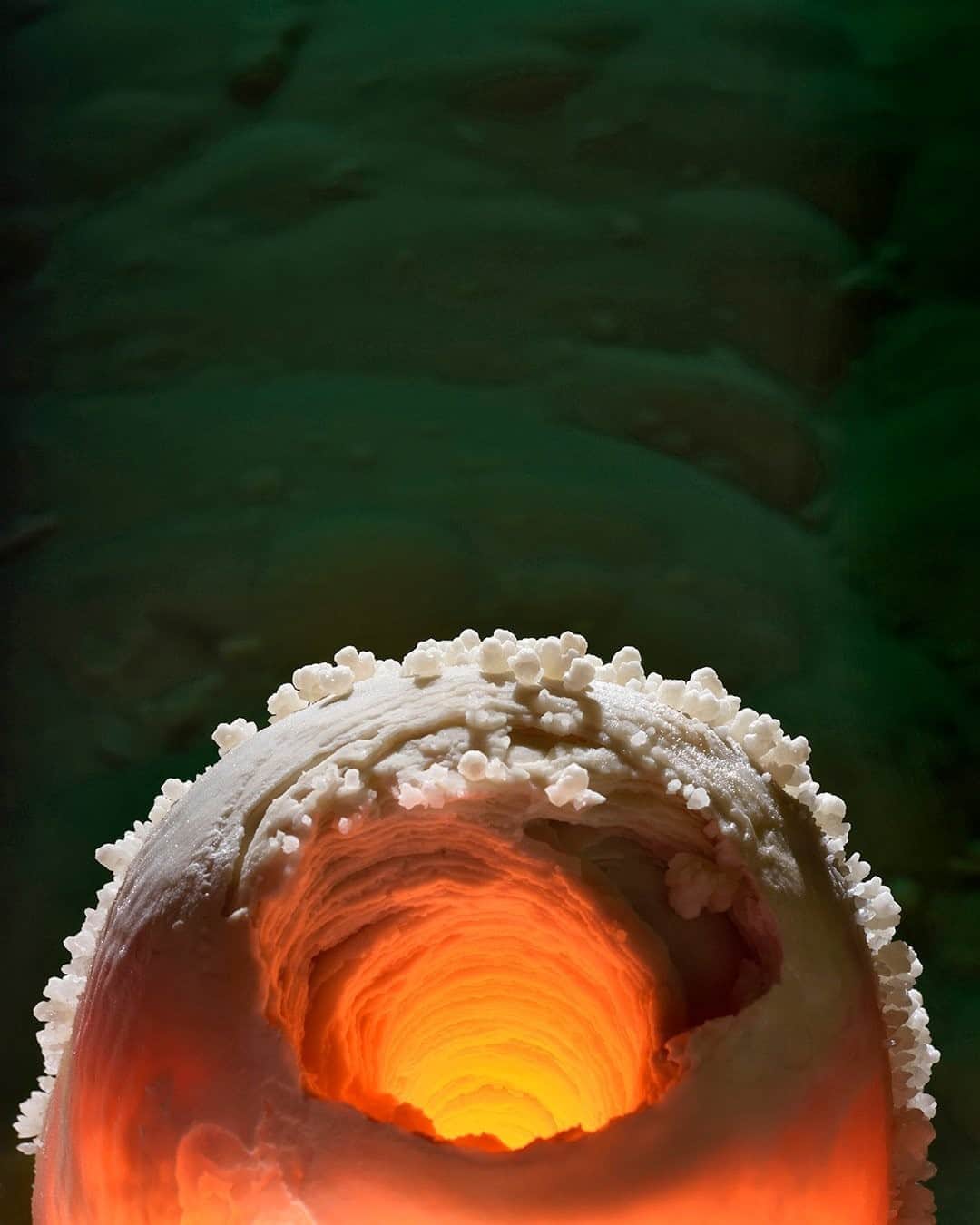 のインスタグラム：「Photo by Robbie Shone @shonephoto  Lechuguilla Cave, in Carlsbad Caverns National Park, offers many wondrous sights.  We illuminated this stalagmite from the outside, giving it a warm, orange glow. What is most unusual about this stalagmite is the hole in the middle. It's very rare and is probably formed when a drop of more acidic water falls from the ceiling and erodes the inside of the stalagmite.」