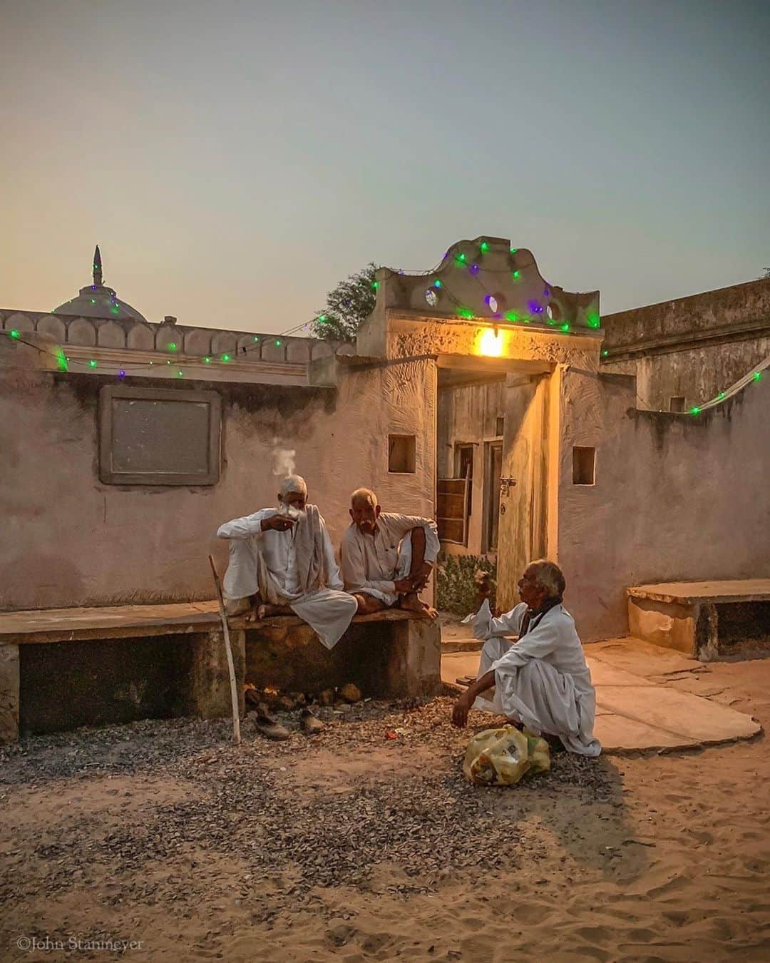 のインスタグラム：「What if that evening in Harasar I hadn’t gone for a walk around the corner from an old fortress we were staying? That moment so brief when the sun comes together with lights and objects created by us. It reminded me that everything we see not from nature exists because they first appeared in someone’s imagination...the Hindu temple, green twinkly lights, cigarettes, the smoke. Even their graceful clothing exists because it was envisioned. I think of such reasoning often these days, and I thought about this when in Rajasthan, India, I came upon elder gentlemen quietly talking. Each naturally placed within the stage we’ve created, that it’s all so real. Thankful having gone for a wander or I never would have met these three men dressed in white. ⠀⠀⠀⠀⠀⠀⠀ India’s Daunting Challenge: There’s Water Everywhere, And Nowhere - Chapter 8 of the @outofedenwalk, my latest story last months (August 2020) issue of @natgeo magazine. ⠀⠀⠀⠀⠀⠀⠀ #twilight #hindu #temple, #hindutemple #green #lights #mentalking #cigarette #smoking #harasar #rajasthan #india @natgeo @outofedenwalk #walkingindia #edenwalk」
