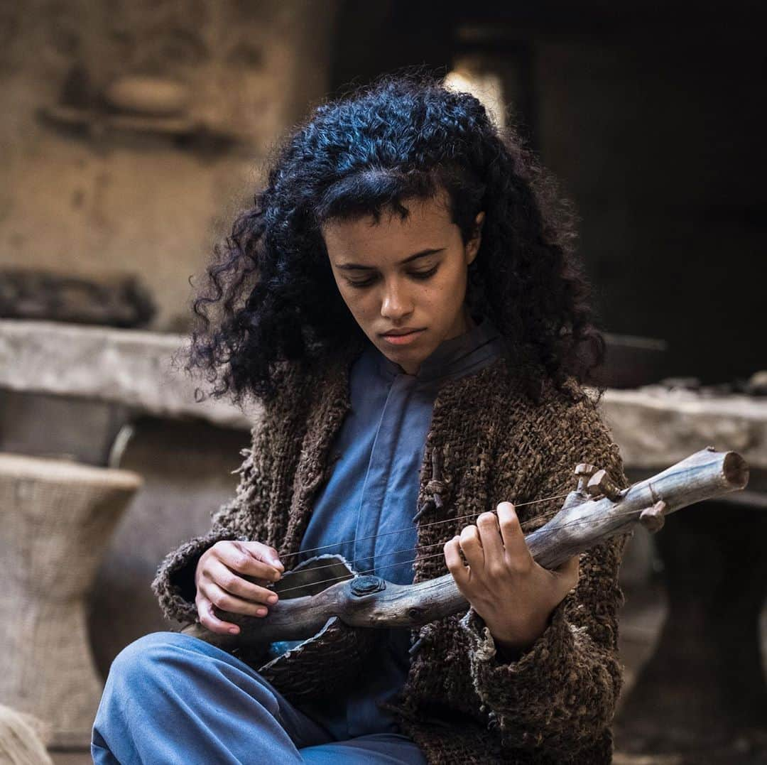 ジョーダン・ロクランのインスタグラム：「Practising hard.  New episodes of @raisedwolvesmax available this Thursday on @hbomax. [Image description: Tempest is sat on a stool, playing a small guitar-like instrument made of pieces of wood. There is a look of concentration on her face.] #RaisedByWolvesMax#HBOMax」