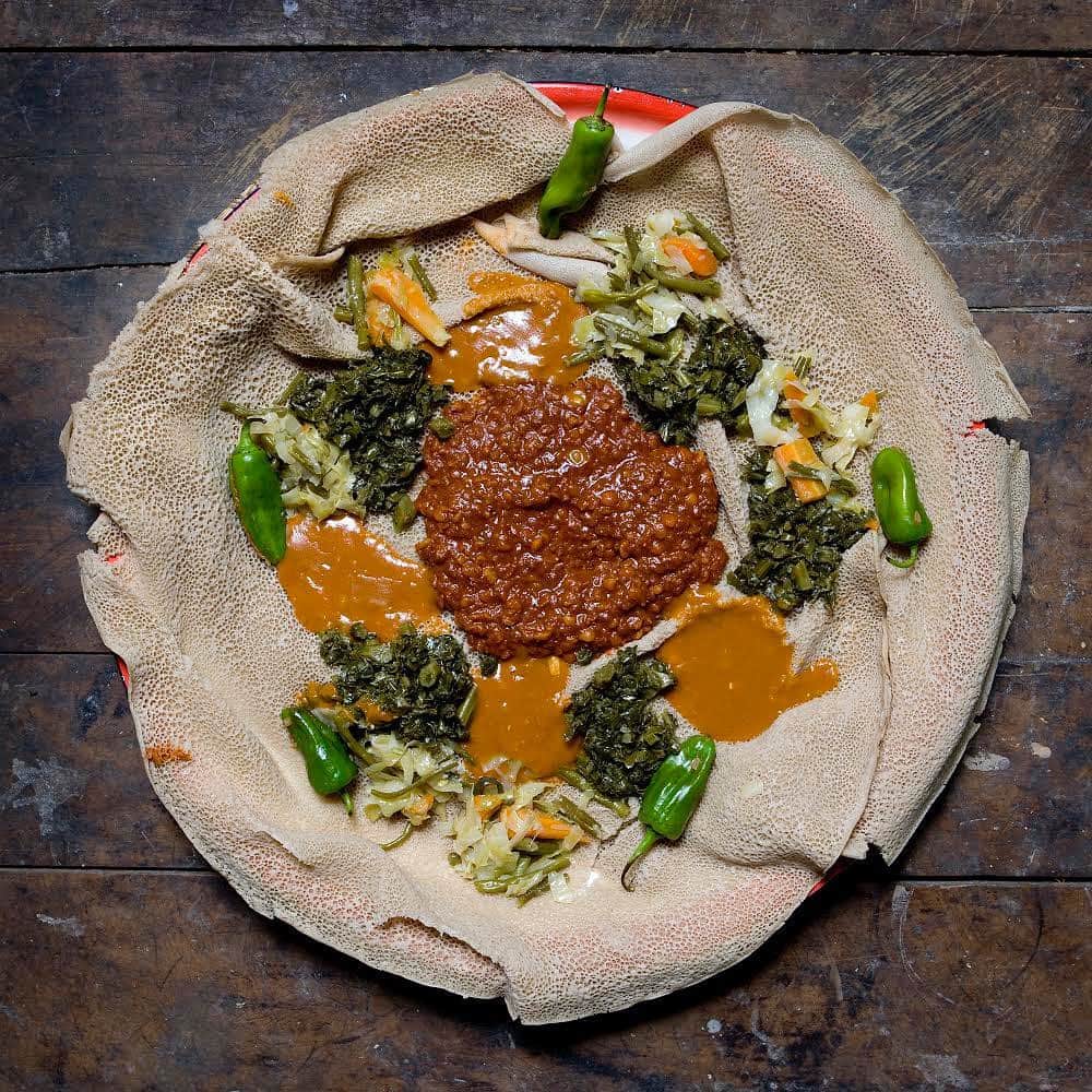 thephotosocietyさんのインスタグラム写真 - (thephotosocietyInstagram)「Photos by @gabrielegalimbertiphoto - From my project GRANDMA'S RECIPES. Bisrat Melake, 60 - Addis Ababa, Ethiopia / ENJERA WITH CHURRY AND VEGETABLES- Difficulty: medium - Time: 3 days (if you need to prepare the enjera), less than 2 hours if the enjera is already ready - Ingredients: 1 savoy, 10 sweet green chillies and 25 string beans, red chilli powder, 4 onions, oil, salt, pepper, cauliflower leaves, a plate of Mitin Shuro (yellow dried peas powder), a plate of split peas, yeast, Teff flour (cereal from Ethiopia) / To prepare this dish you need to cook different ingredients separately. It is the product of various recipes. The Enjara, whose preparation takes 3 days, is the first thing to make: ENJARA: Mix 1 kilo of teff flour and 1 spoon of yeast with some water until you obtain a smooth and dense dough - let it ferment for 3 days - now the dough should be much softer than when you prepared it 3 days before. Add water until it becomes cream-like. Use it in the same way as when you make crepes. If you have the possibility to use an Ethiopian oven in ceramic (like the ones at her back in the photo), do use it! / CHURRY (in the centre of the photo): Stir fry 3 chopped onions and 10 chopped sweet chillies in some oil for a few minutes. Add 3 glasses of water and let it cook for about ten minutes. Then, add the split peas and the plate of Mitin Shuro. Mix well, cover with a lid and cook on a low heat for about 30 minutes / CAULIFLOWER LEAVES (the dark green vegetables on the sides of the photo): Boil some cauliflower leaves in water. Drain and chop them and fry them in a pan with some oil, onion and salt / LIQUID CHURRY (the small orange spots in the photo): Fry lightly half an onion and a pinch of hot chili powder in some oil. Add 200 grams of Mitin Shuro and two glasses of water. Cook for 20 minutes / STRING BEANS AND SAVOY SALAD: Slice the savoy into stripes and chop the beans. Boil everything together in some water to suit your taste. Drain the vegetables and put them in a pan with oil and chili to sauté them for about ten minutes / Now that all the ingredients are ready, you can place them in the dish as it is shown in the photo and serve it. #grandma」9月23日 1時35分 - thephotosociety