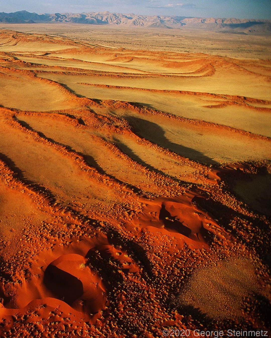 ナショナルジオグラフィックさんのインスタグラム写真 - (ナショナルジオグラフィックInstagram)「Photo by George Steinmetz @geosteinmetz / Youcan judge the age of a desert by its color, as it takes thousands of years for the iron minerals of each sand grain to oxidize into a ripe orange. The dunes of the Namib are among the oldest on Earth and stabilized by colonies of grass that are nurtured by the coastal fog and its dew. These are fragile ecosystems, with living cryptobiotic soils. They can be scarred by careless car tracks, but are now protected by a strict legal system that preserves them in perpetuity. To explore more of our world from above, follow @geosteinmetz.」10月27日 23時42分 - natgeo