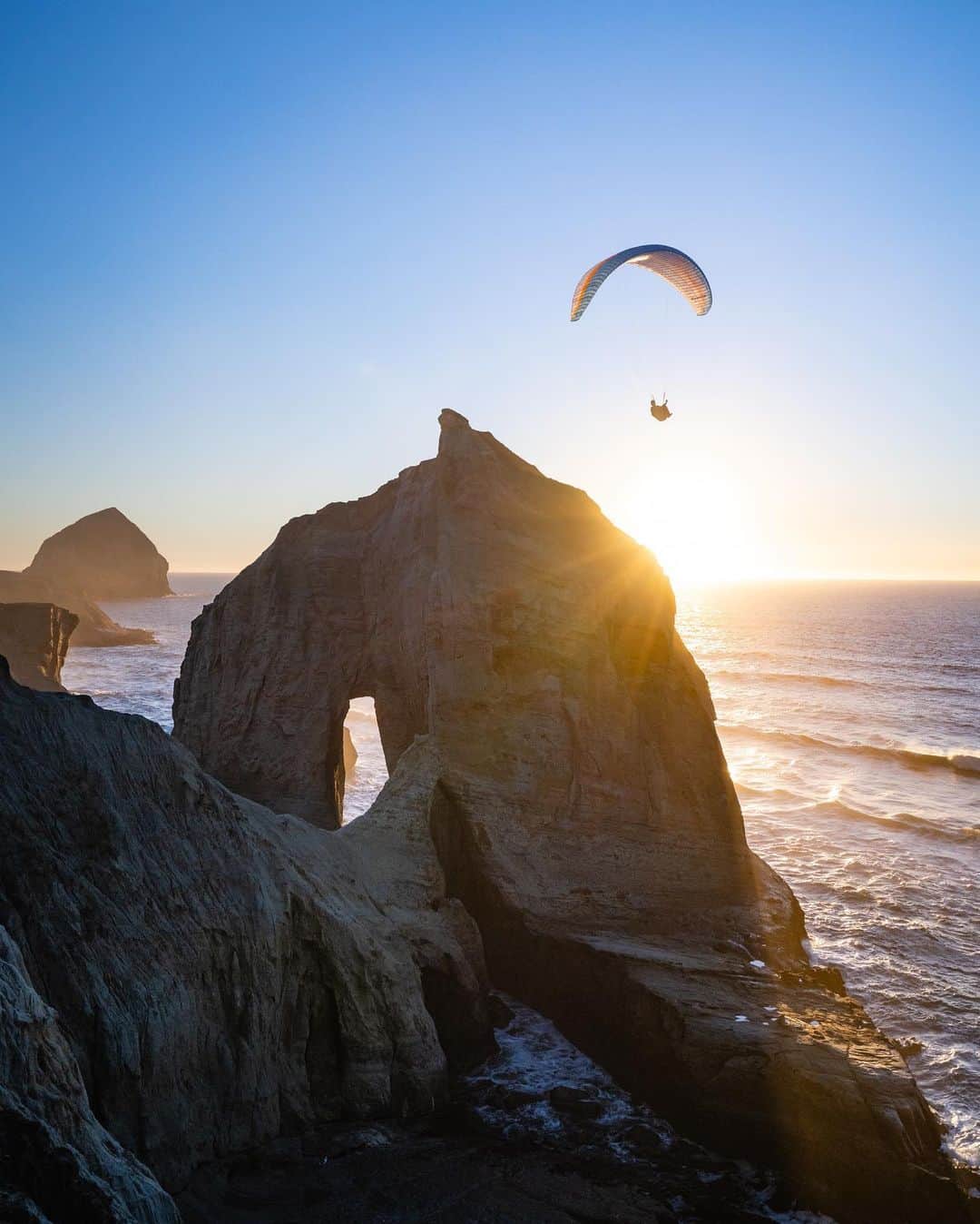 Travis Burkeのインスタグラム：「My flight last night over the incredible Oregon Coast 😍. What a breathtaking way to experience different places as we travel!  What’s even more crazy is that the same wind that allowed me to fly was making perfectly groomed waves break all day on the other side of the dunes! I landed with just enough time to witness the last set being kissed by light.  Thanks to @gypsealaysea for capturing the photos of me and to @ozoneparagliders for helping make my dream of flying a reality!🦅🙌🏼   #flying #paragliding #oregon #pnw」