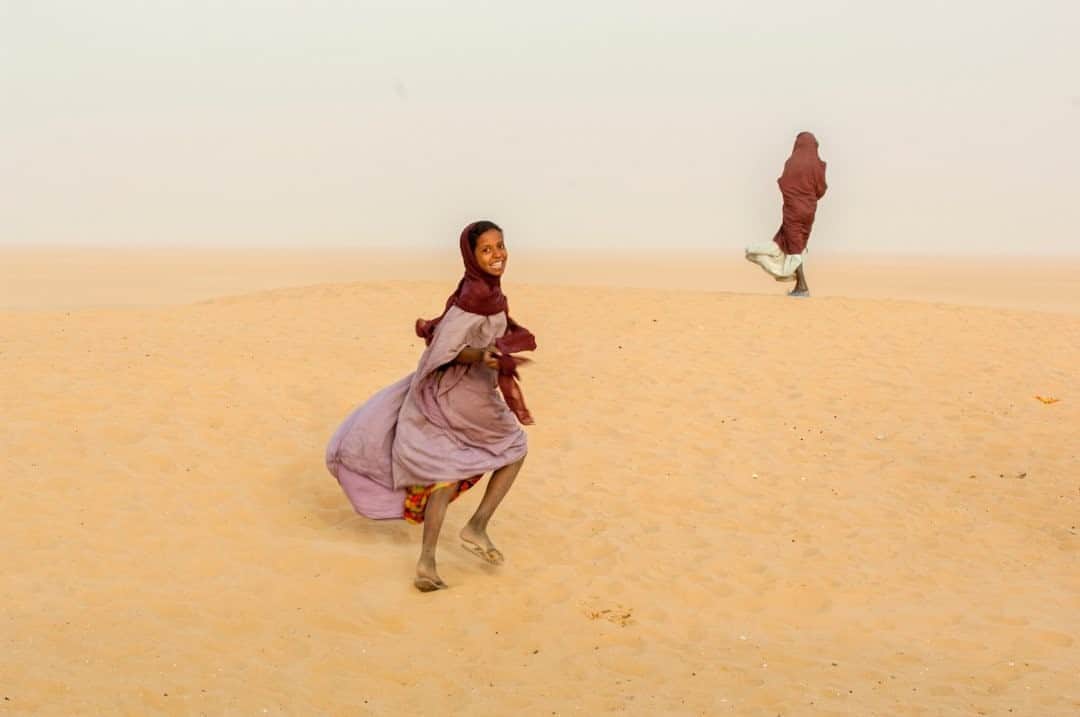 ナショナルジオグラフィックさんのインスタグラム写真 - (ナショナルジオグラフィックInstagram)「Photo by @amivitale / This image is meant to celebrate the International Day of the Girl. Here, girls run from a sandstorm in the remote desert town of Boujbeja, Mali. "Boujbeja" means the luck of the desert, but after a severe drought in 1966, they've been fighting the constant push of the sands and must dig 70 meters underground to get water. As the climate changes, and earth grows hotter, droughts are becoming more severe, making the quest for water more and more difficult. Finding water is a task that disproportionately falls to women and girls. Collectively they spend 200 million hours every single daily seeking and hauling water for their communities, a task that steals their time and potential, which is why it's so important to support groups and organizations that make access to clean water a priority. Follow @amivitale for more photos celebrating the hope and beauty in the world. @thephotosociety @rippleeffectimages #DayOfTheGirl #girls #climatechange #mali #desert」10月11日 23時37分 - natgeo