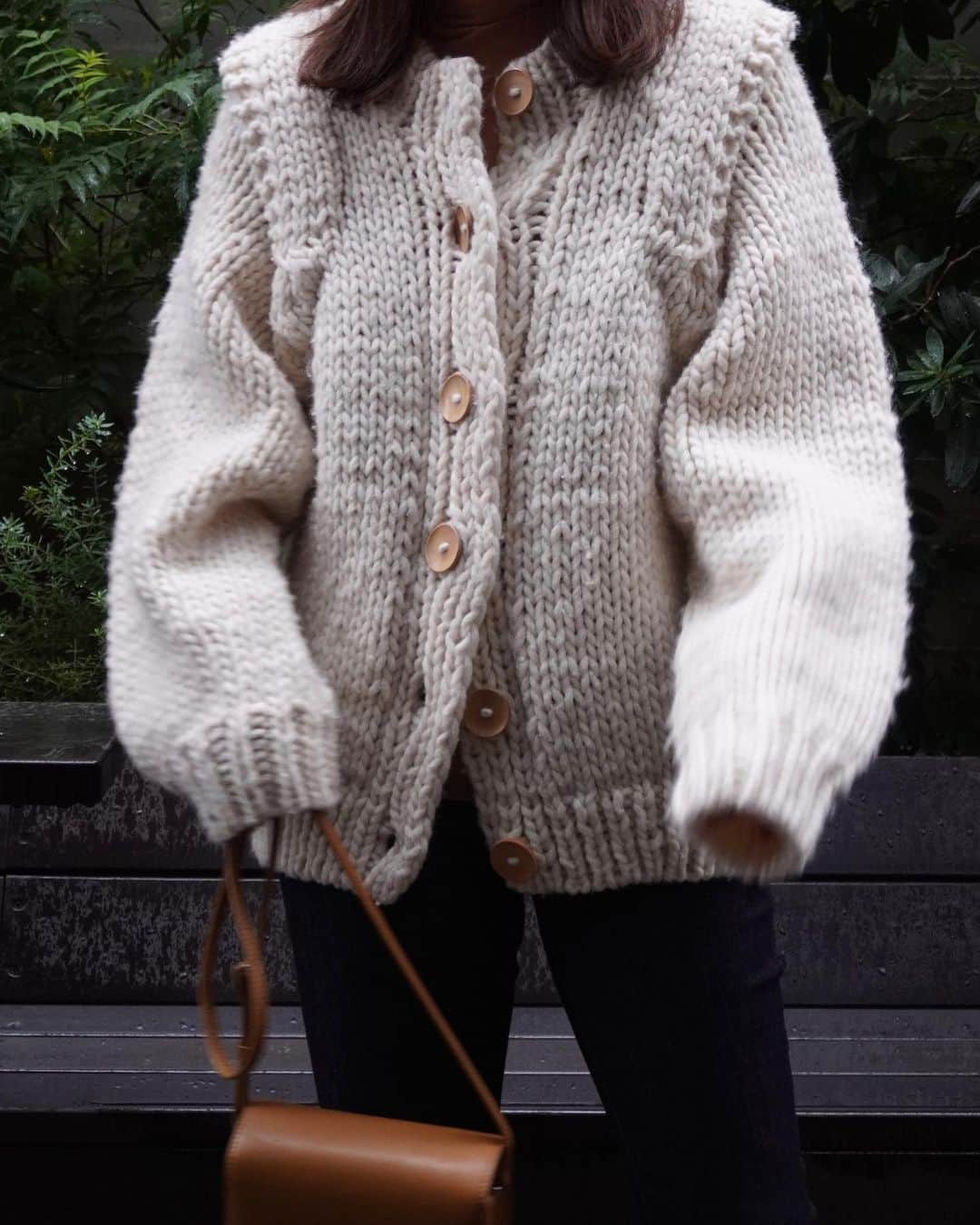 JUNNAのインスタグラム：「大きなウッドボタンと ショルダーのタックデザインが気に入ってる...🧶  ニットの中でも特に好きなペルーニット  一点一点手編みならではの風合い、無骨感 ちょっと昔懐かしい雰囲気の漂う  #ショルダータックハンドニットカーデ  今日はバレエシューズとバッグとウッドボタンの 色をあわせたスタイリング  着用後には毎回軽く馬の毛ブラシでブラッシング スチーマーを当てると抗菌効果も◎  網目が伸びたらスチーマーを当てて 新品状態を長く楽しみながら愛用しています  詳しいhow toはYouTubeで準備中です✨」