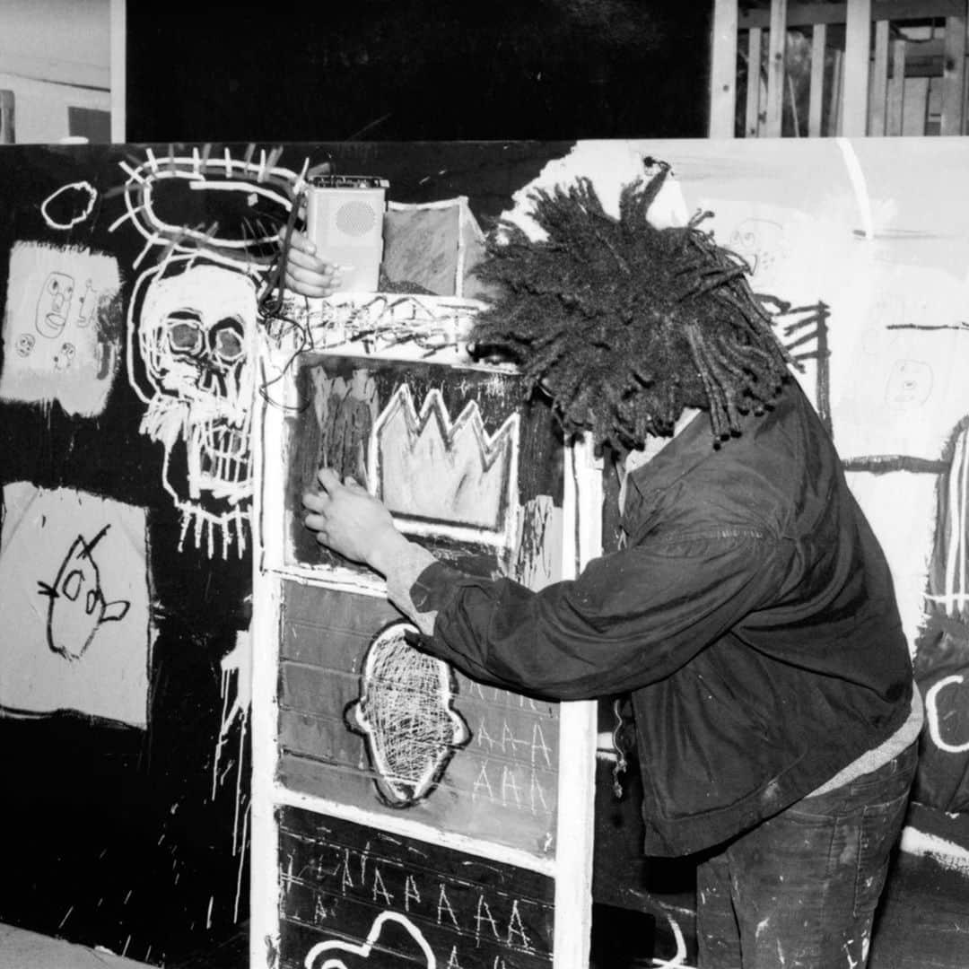 サザビーズさんのインスタグラム写真 - (サザビーズInstagram)「📸: Snapped here is Jean-Michel Basquiat side-by-side with his work ‘Minor Success’ at Annina Nosei Gallery in 1982. Dating to the very earliest phase in the artist’s career, the work was created two years prior and features three of what would become the artist’s most iconic motifs – 🚗 💀 👑 – drawn on the surface of a mirrored cupboard door.   1980 was a watershed moment for #Basquiat. Following his participation in ‘The Times Square Show’, the young artist was then invited to exhibit as part of the ‘New York / New Wave’ at @momaps1, asking a then teenage Basquiat, at that time listed under the name SAMO, to create a bold installation of some 20 paintings.    ‘Minor Success’ is currently on display in our #London galleries alongside the artist’s ‘Justcome Suit’ from 1983, both of which will be offered on Wednesday in #SothebysContemporary Art livestreamed auction.   Pulsating with urban rhythm, 👉 to see the frenetic ‘Justcome Suit’ composition swathed with a myriad of references that evoke the language of NYC in disarray.  © The Estate of Jean-Michel Basquiat / ADAGP, Paris and DACS, London 2020」10月17日 17時04分 - sothebys