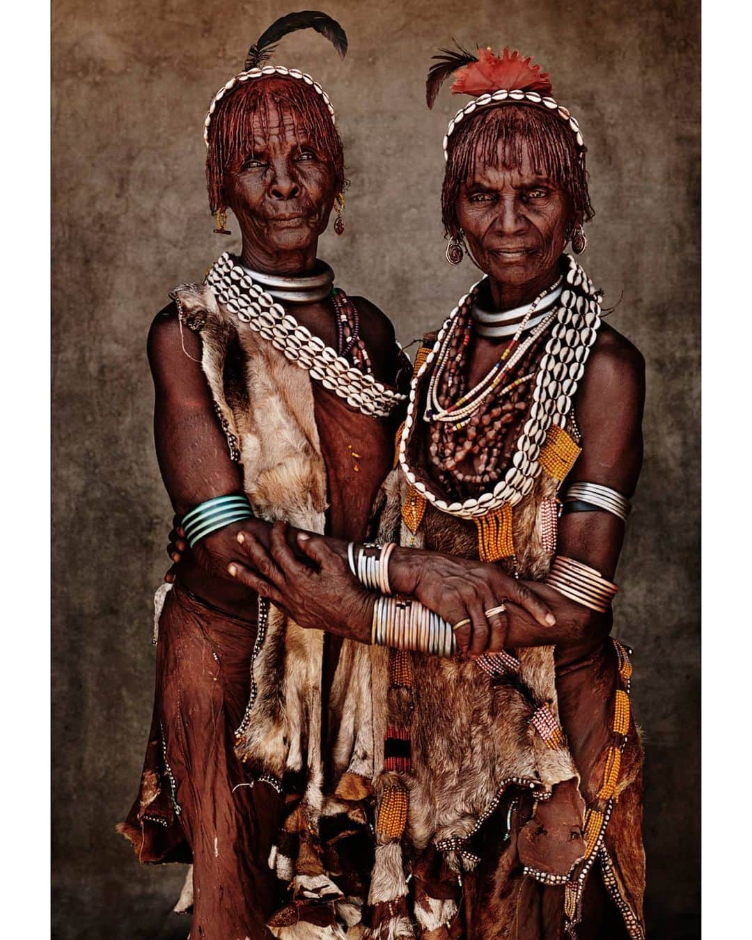 マリオ・テスティーノのインスタグラム：「Encountering these ladies, while visiting a Hamar community in Ethiopia, was an amazing surprise. Surrounded by beautiful young women, their faces were unmatched; beautiful and full of stories. As older Hamar women, they wore additional decoration only meant for people their age. The red clay they apply to their hair and skin and the redish of their clothes create a wonderful hue. Despite the language barrier I could tell they were a central part of their community, two women with much to say and to share.   _ Encontrar a estas mujeres, mientras visitaba una comunidad Hamar en Etiopía, fue una sorpresa increíble. Rodeadas de jóvenes bellas, sus rostros eran inigualables, hermosos y llenos de historias. Como mujeres Hamar mayores, usan adornos que las caracterizan como personas de su edad. La arcilla roja que aplican a su cabello y piel y el rojizo de su ropa crean una tonalidad maravillosa. A pesar de la barrera del idioma, me di cuenta de que son una parte central de su comunidad, dos mujeres con mucho que decir y compartir.  #ABeautifulWorld #MarioTestino #2019」