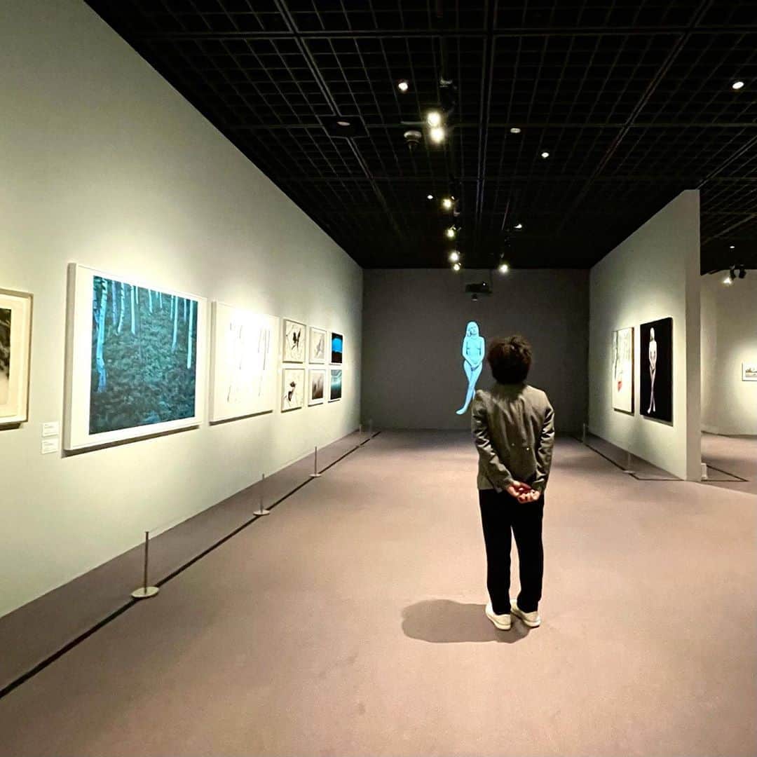 林信行のインスタグラム：「100人の写真家の眼差しを通してみる"東京＝好奇心（キュリオシティ）"をテーマにした写真展がパリ、ベルリンを巡回し、少し遅れたけれど東京の渋谷にて「東京好奇心 2020 渋谷」として明日からスタート！  コロナ 禍でまったく別の意味を持った「Tokyo 2020」で見ておくべき展覧会のひとつと思います。  Tokyo Curiosity 2020: starts tomorrow at Bunkamura, the Museum: a photo exhibition that shows the perspectives on Tokyo through pictures by 100 photographers from around the world.  　展覧会場、一番最初に目に入るのは踏みつけようとするアメリカ兵の靴底の写真。東松照明さんの「チューインガムとチョコレート」。その後に今日、世界を埋め尽くす「プラスチック」というタイトルの作品が続く。その隣には、戦後の同じ頃に、口元に手をそえて笑う日本人女性のしぐさが美しいと"Femmes Japonaises"という写真集を出したフランス人写真家、マーク・リブーさんの作品がつづく。 　この展覧会、最初の章のテーマはTimelessness。 　本展はそれぞれ対をなす４つのテーマ「Identity」と「Diversity」、「Here and Now」と「Timelessness」の４つのキーワードで写真を集め、それを13の章にまとめて展示を行なっている。 　中でももっとも重要なのは「Timessless」だと太田菜穂子さんは言う。「私たちは今という時代を生きているが、過去も現在も未来も色々な形でつながっている。それは、どうつながっているのか…」と問いを投げかける。 　もう１つ重要なのが「私たちは一体何者でどこから来たのか」のアイデンティティーとこれからますます重要になる「多様性」。 　１章の向かいの壁に展示された第２章のテーマは「Identity & Diversity」。多様な日本人のアイデンティティーを感じさせてくれる写真が並ぶ。最初の２枚はアメリカ人写真家、エヴェレット・ケネディー・ブラウンさんによる公家と武家の写真。日本の歴史には常に２層の支配構造があり、それが共存してきた、と太田さん。一番、アイデンティティーを確立しているのは、アーティストだとも付け加える。 　第３章は止まった時間がテーマ。写真とはそもそも動いている時間を止めてしまう装置だが、ここで展示をしているのは戦争によって強制的に止められてしまった時間を移した作品たち。 　本展覧会で、もっとも見応えがあるのは、次の第４章、「花鳥風月」という章で、菅原一剛さんの椿の湿板写真（裏地にはベルベットを使用）で始まり、隣は大和田良さんが、500年以上生きてきた盆栽を１年以上の時間をかけて撮り合成した写真、香港のセリン・ウーさんの樹木の影を人間国宝がつくった越前和紙にインクジェットで印刷した作品がつづく。 　中央には瀧本幹也さんが長野県小諸市にあるルイ・ヴィトンの森の夏と冬を撮った作品。日本の豊かな自然を絵画的かつ繊細な形で捉えた作品だ。友人で本展のアートディレクターを務める柿木原政広さんに言われて気がついたが作品の上下の余白の幅までこだわって調整した繊細な作品だ。 　宇壽山貴久子さんによる代々木公園のカラスと桜の作品。代々木公園は、公園に生息するさまざまな生物の図鑑を用意しているが、カラスは差別され、その図鑑に載っていないことに着目して作品を撮り始めたと言うが、大変、忌み嫌われているカラスが桜との共演で美しい写真作品にまとまっている。 　一番奥には、こくまい太さんとゴトー・アキさんによる日本の山紫水明の美しさを感じさせる写真。 　そしてその向かいには太田さんが今、一番美しいヌード作品と評する上田義彦さんの大きな写真が２点。 　１点は色素が欠落したアルビノの女性のヌードを撮った写真で、どこか現実離れした実写ではないような雰囲気を漂わせる。これも柿木原さんに教えてもらったのだが、この写真がちゃんと現実だとわかるように、写真の左下にはあえて映り込んだ三脚の足を残してあった。 　ここから世界中のアーティストに愛された日本の写真家、鋤田（すきた）正義さんによる有名なデビッド・ボウイの写真（東京好奇心のベルリン展でメインビジュアルになった）など有名作品含め膨大な数の作品がギャラリーを埋めており、かなりの見応えがある。 　2018年、渋谷のヒカリエで始まり、2019年にパリとベルリンで開催、そして今年、オリンピックの前に凱旋して開催されるはずだった本展は、予定より５ヶ月ほど遅れての開催となったが、参加作家もボードメンバーやスポンサーも気合は十分で、そのことはこだわりのカタログからも伝わってくる(文字数制限で書ききれないので、詳細はFacebook投稿を参照)  展覧会の撮影は禁止で本投稿は特別な許可を得て撮影している。  東京好奇心 2020 渋谷 Bunkamura ザ・ミュージアム 2020/10/20（火）-11/12（木） 会期中無休 #東京好奇心　#bunkamuraザミュージアム #渋谷」