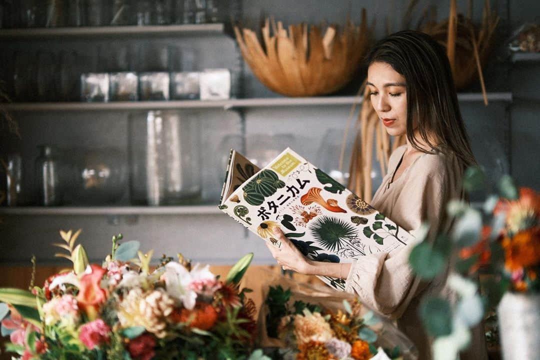 磯部映見のインスタグラム：「わーい素敵な写真を撮ってもらいました。  Loving the soft autumn light & shadow in our studio. Flowers can bring Autumn straight into your home. 🍁  Thank you @ramon_onizawa 📷  @hanatombo のアトリエも、だんだんと年季が入ってきたけど、暖かい光が入るのは変わらず気に入ってるところ。  また子どもから大人まで皆さまとここで手を動かしたいけど、小さな空間なのでもう少しお預けです💐  #hanatombo #floralart #フラワーアート　#アトリエ　#thewagon  (#この本は読んでる風😆)」