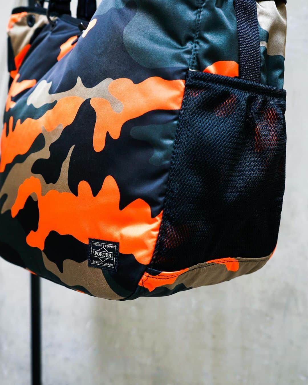 のインスタグラム：「.﻿ SHOP ORIGINAL﻿ PS CAMO﻿ ﻿ ウッドランドパターンのカモフラージュ柄に、ビビットなオレンジカラーを取り入れたPORTER STANDオリジナルシリーズ。﻿ ﻿ サイドに設けたペットボトルや折り畳み傘が収納可能なメッシュポケットや内装のPC専用ポケットなど充実した収納が特徴です。﻿ ﻿ 2WAY TOTE BAG﻿ No.384-08300﻿ ￥29,500+tax﻿ W350/H370/D180mm﻿ ﻿ #yoshidakaban #porter #luggagelabel #madeinjapan #japan #porterstand #shinagawa #tokyo #kyoto #ps #camo #totebag #limited #exclusive #吉田カバン#ポーター #ポータースタンド #品川 #東京 #京都 #カモフラージュ #トートバッグ」