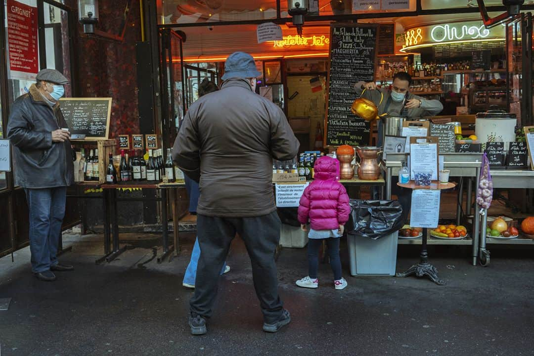 ルモンドさんのインスタグラム写真 - (ルモンドInstagram)「La rue de Belleville, à Paris, accueille paresseusement ses habitués du samedi matin. Au bar des Folies, les réguliers sont à peine perturbés par la transformation de l’institution du quartier en épicerie-pizzeria. « On est des caméléons. On regarde tous les jours ce qu’on a le droit de faire, et on s’adapte », s’amuse presque le serveur. Ce n’est pas pour déplaire à Khalil Ghabara, qui continue à venir tous les matins, « comme avant ». Il sort plusieurs fois par jour, usant d’une attestation puis d’une autre. « Mais toujours en règle ! »⁣ Les stores baissés se font de plus en plus rares en remontant la rue, et les trottoirs se gorgent de badauds. Un couple s’arrête devant une papeterie, ouverte elle aussi. « Dis, chéri, on ne rentrerait pas là ? On n’y est jamais allés ! » Boulanger, boucher, poissonnier, fromager… Les files s’étirent, moins longues que lors du premier confinement mais pleines toute la journée. « Est-ce que c’est très raisonnable ? Je ne sais pas », convient Sabine Civilise en attendant son tour – « J’avais envie de lapin ! » – à la boucherie.⁣ La boutique vide et l’air contrarié, Mahnaz la chocolatière observe la rue débordant de vie en soupirant. « Les gens sont des enfants, les policiers sont occupés ailleurs, alors, ils en profitent pour passer entre les gouttes… » En Iran, Mahnaz a connu la guerre, puis l’embargo. « Du coup quand les gens disent : “J’en ai marre d’être confiné”, alors que les rayons des magasins sont pleins, je préfère ne rien dire… » Sans en penser moins.⁣ -⁣ 1 : Le café des Folies s’est reconverti momentanément en pizzeria-traiteur pour contourner les mesures de fermeture⁣ 2 : Foued, peintre, boit un café rue de Belleville, le 7 novembre⁣ 3 : Les files d’attentes devant les commerces de bouche de la rue de Belleville⁣ 4 : Davy et Stéphane, après avoir fait la fête toute la nuit chez des amis, sont à la recherche d’huîtres et de vin blanc sur le marché⁣ 5 : Mahnaz, dans sa boutique de chocolats⁣ 6 : Sophie et Brigitte partagent leur café du matin devant l’église de Belleville⁣ 7 : La rue de Belleville à Paris le 7 novembre⁣ -⁣ Photos : Agnès Dherbeys (@agnes_dherbeys) #PourLeMonde⁣ -⁣ #covid #coronavirus #commerce」11月11日 22時42分 - lemondefr