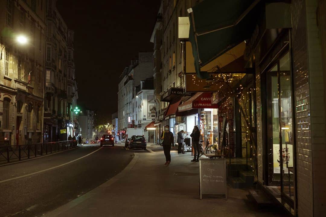 ルモンドさんのインスタグラム写真 - (ルモンドInstagram)「La rue de Belleville, à Paris, accueille paresseusement ses habitués du samedi matin. Au bar des Folies, les réguliers sont à peine perturbés par la transformation de l’institution du quartier en épicerie-pizzeria. « On est des caméléons. On regarde tous les jours ce qu’on a le droit de faire, et on s’adapte », s’amuse presque le serveur. Ce n’est pas pour déplaire à Khalil Ghabara, qui continue à venir tous les matins, « comme avant ». Il sort plusieurs fois par jour, usant d’une attestation puis d’une autre. « Mais toujours en règle ! »⁣ Les stores baissés se font de plus en plus rares en remontant la rue, et les trottoirs se gorgent de badauds. Un couple s’arrête devant une papeterie, ouverte elle aussi. « Dis, chéri, on ne rentrerait pas là ? On n’y est jamais allés ! » Boulanger, boucher, poissonnier, fromager… Les files s’étirent, moins longues que lors du premier confinement mais pleines toute la journée. « Est-ce que c’est très raisonnable ? Je ne sais pas », convient Sabine Civilise en attendant son tour – « J’avais envie de lapin ! » – à la boucherie.⁣ La boutique vide et l’air contrarié, Mahnaz la chocolatière observe la rue débordant de vie en soupirant. « Les gens sont des enfants, les policiers sont occupés ailleurs, alors, ils en profitent pour passer entre les gouttes… » En Iran, Mahnaz a connu la guerre, puis l’embargo. « Du coup quand les gens disent : “J’en ai marre d’être confiné”, alors que les rayons des magasins sont pleins, je préfère ne rien dire… » Sans en penser moins.⁣ -⁣ 1 : Le café des Folies s’est reconverti momentanément en pizzeria-traiteur pour contourner les mesures de fermeture⁣ 2 : Foued, peintre, boit un café rue de Belleville, le 7 novembre⁣ 3 : Les files d’attentes devant les commerces de bouche de la rue de Belleville⁣ 4 : Davy et Stéphane, après avoir fait la fête toute la nuit chez des amis, sont à la recherche d’huîtres et de vin blanc sur le marché⁣ 5 : Mahnaz, dans sa boutique de chocolats⁣ 6 : Sophie et Brigitte partagent leur café du matin devant l’église de Belleville⁣ 7 : La rue de Belleville à Paris le 7 novembre⁣ -⁣ Photos : Agnès Dherbeys (@agnes_dherbeys) #PourLeMonde⁣ -⁣ #covid #coronavirus #commerce」11月11日 22時42分 - lemondefr