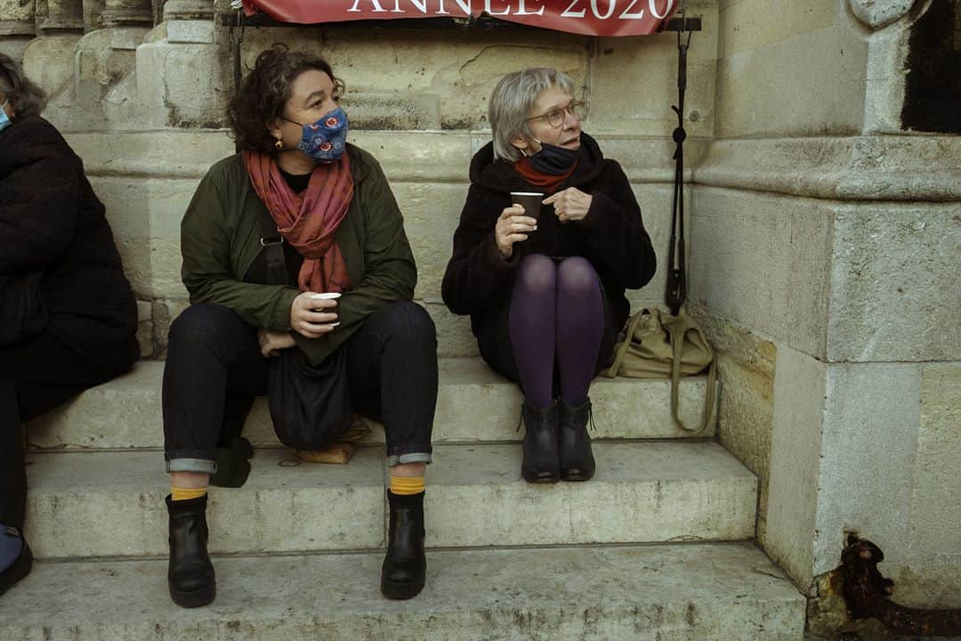 ルモンドさんのインスタグラム写真 - (ルモンドInstagram)「La rue de Belleville, à Paris, accueille paresseusement ses habitués du samedi matin. Au bar des Folies, les réguliers sont à peine perturbés par la transformation de l’institution du quartier en épicerie-pizzeria. « On est des caméléons. On regarde tous les jours ce qu’on a le droit de faire, et on s’adapte », s’amuse presque le serveur. Ce n’est pas pour déplaire à Khalil Ghabara, qui continue à venir tous les matins, « comme avant ». Il sort plusieurs fois par jour, usant d’une attestation puis d’une autre. « Mais toujours en règle ! »⁣ Les stores baissés se font de plus en plus rares en remontant la rue, et les trottoirs se gorgent de badauds. Un couple s’arrête devant une papeterie, ouverte elle aussi. « Dis, chéri, on ne rentrerait pas là ? On n’y est jamais allés ! » Boulanger, boucher, poissonnier, fromager… Les files s’étirent, moins longues que lors du premier confinement mais pleines toute la journée. « Est-ce que c’est très raisonnable ? Je ne sais pas », convient Sabine Civilise en attendant son tour – « J’avais envie de lapin ! » – à la boucherie.⁣ La boutique vide et l’air contrarié, Mahnaz la chocolatière observe la rue débordant de vie en soupirant. « Les gens sont des enfants, les policiers sont occupés ailleurs, alors, ils en profitent pour passer entre les gouttes… » En Iran, Mahnaz a connu la guerre, puis l’embargo. « Du coup quand les gens disent : “J’en ai marre d’être confiné”, alors que les rayons des magasins sont pleins, je préfère ne rien dire… » Sans en penser moins.⁣ -⁣ 1 : Le café des Folies s’est reconverti momentanément en pizzeria-traiteur pour contourner les mesures de fermeture⁣ 2 : Foued, peintre, boit un café rue de Belleville, le 7 novembre⁣ 3 : Les files d’attentes devant les commerces de bouche de la rue de Belleville⁣ 4 : Davy et Stéphane, après avoir fait la fête toute la nuit chez des amis, sont à la recherche d’huîtres et de vin blanc sur le marché⁣ 5 : Mahnaz, dans sa boutique de chocolats⁣ 6 : Sophie et Brigitte partagent leur café du matin devant l’église de Belleville⁣ 7 : La rue de Belleville à Paris le 7 novembre⁣ -⁣ Photos : Agnès Dherbeys (@agnes_dherbeys) #PourLeMonde⁣ -⁣ #covid #coronavirus #commerce」11月11日 22時42分 - lemondefr