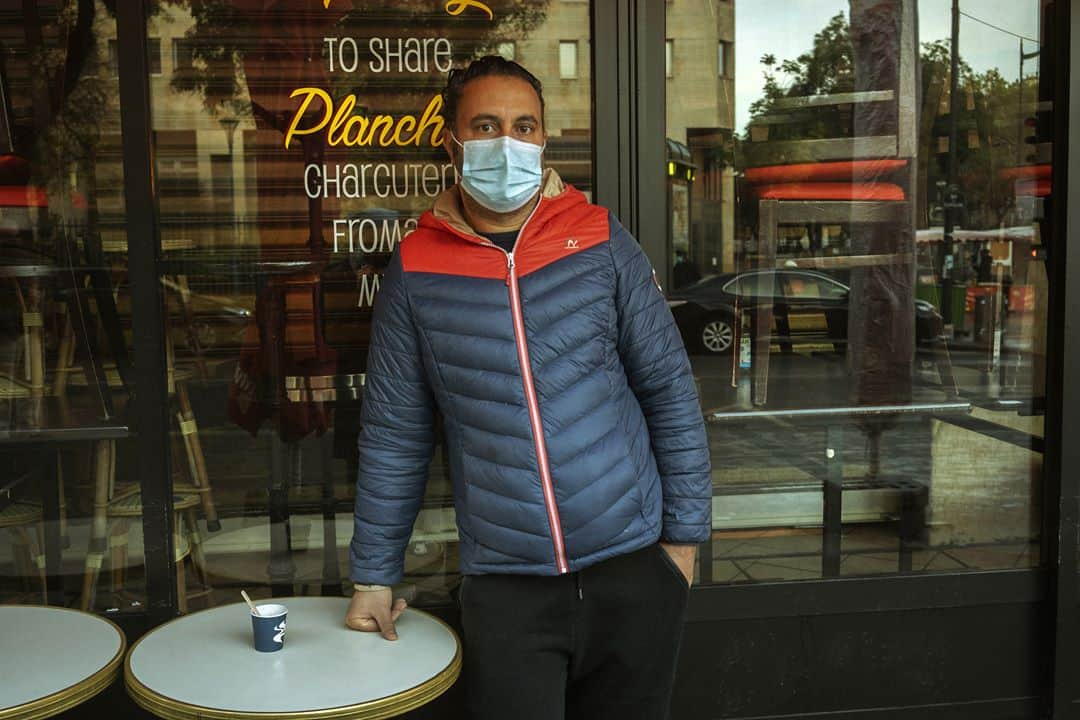 ルモンドさんのインスタグラム写真 - (ルモンドInstagram)「La rue de Belleville, à Paris, accueille paresseusement ses habitués du samedi matin. Au bar des Folies, les réguliers sont à peine perturbés par la transformation de l’institution du quartier en épicerie-pizzeria. « On est des caméléons. On regarde tous les jours ce qu’on a le droit de faire, et on s’adapte », s’amuse presque le serveur. Ce n’est pas pour déplaire à Khalil Ghabara, qui continue à venir tous les matins, « comme avant ». Il sort plusieurs fois par jour, usant d’une attestation puis d’une autre. « Mais toujours en règle ! »⁣ Les stores baissés se font de plus en plus rares en remontant la rue, et les trottoirs se gorgent de badauds. Un couple s’arrête devant une papeterie, ouverte elle aussi. « Dis, chéri, on ne rentrerait pas là ? On n’y est jamais allés ! » Boulanger, boucher, poissonnier, fromager… Les files s’étirent, moins longues que lors du premier confinement mais pleines toute la journée. « Est-ce que c’est très raisonnable ? Je ne sais pas », convient Sabine Civilise en attendant son tour – « J’avais envie de lapin ! » – à la boucherie.⁣ La boutique vide et l’air contrarié, Mahnaz la chocolatière observe la rue débordant de vie en soupirant. « Les gens sont des enfants, les policiers sont occupés ailleurs, alors, ils en profitent pour passer entre les gouttes… » En Iran, Mahnaz a connu la guerre, puis l’embargo. « Du coup quand les gens disent : “J’en ai marre d’être confiné”, alors que les rayons des magasins sont pleins, je préfère ne rien dire… » Sans en penser moins.⁣ -⁣ 1 : Le café des Folies s’est reconverti momentanément en pizzeria-traiteur pour contourner les mesures de fermeture⁣ 2 : Foued, peintre, boit un café rue de Belleville, le 7 novembre⁣ 3 : Les files d’attentes devant les commerces de bouche de la rue de Belleville⁣ 4 : Davy et Stéphane, après avoir fait la fête toute la nuit chez des amis, sont à la recherche d’huîtres et de vin blanc sur le marché⁣ 5 : Mahnaz, dans sa boutique de chocolats⁣ 6 : Sophie et Brigitte partagent leur café du matin devant l’église de Belleville⁣ 7 : La rue de Belleville à Paris le 7 novembre⁣ -⁣ Photos : Agnès Dherbeys (@agnes_dherbeys) #PourLeMonde⁣ -⁣ #covid #coronavirus #commerce」11月11日 22時42分 - lemondefr