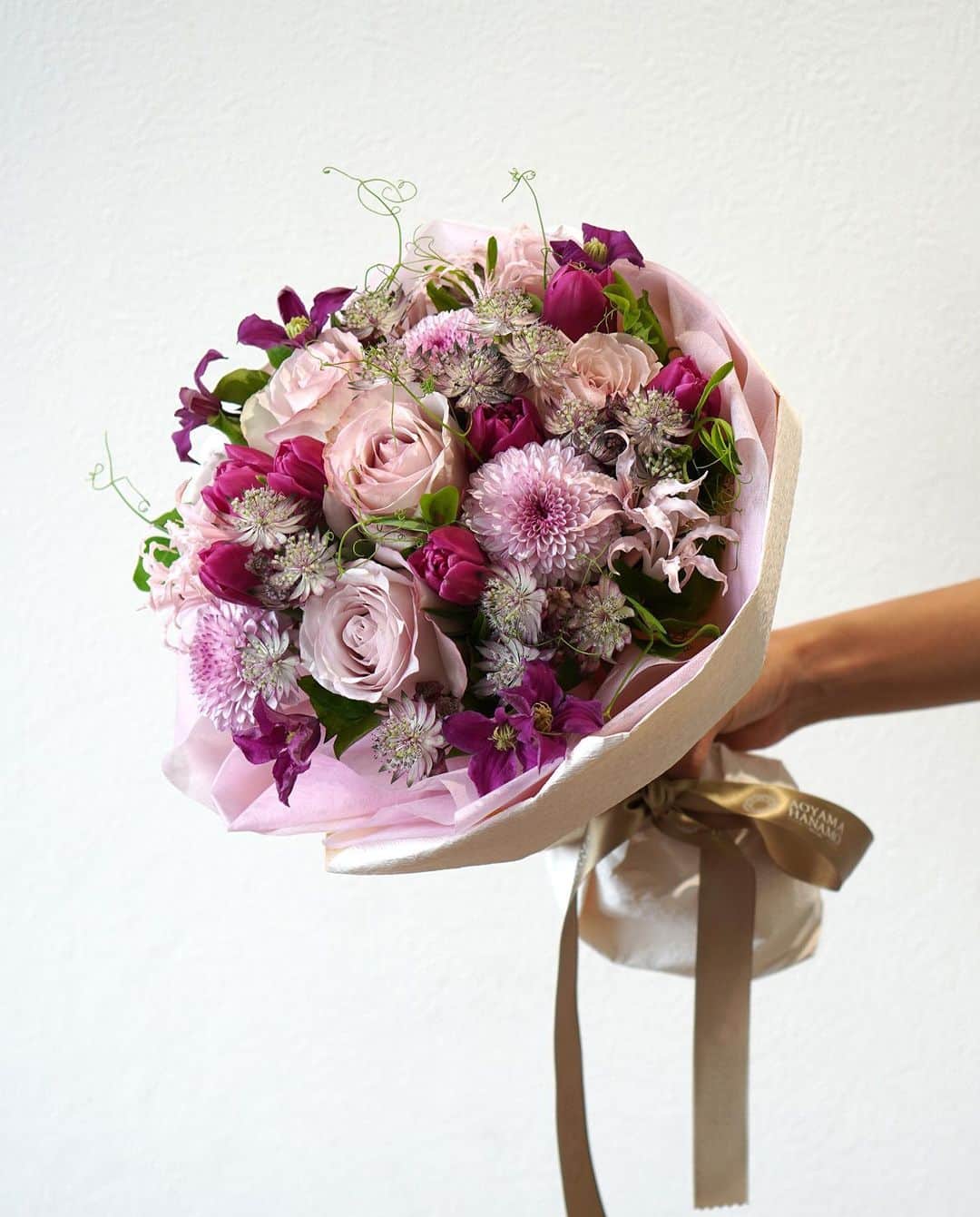 のインスタグラム：「ラウンドスタイルのおまかせブーケ。 ・ さまざまな種類のピンクや紫の花をふんだんに使い、 花色のグラデーションが美しい仕上がりに。 動きのあるリーフがナチュラルさを加えています。 - - - #aoyamahanamo #flowers #flowershop #florist #instaflower #flowergram #flowerstagram #flowerlovers #おまかせ花束  #おまかせブーケ #青山花茂おまかせブーケ #バラ #チューリップ #アストランジア #クレマチス #ネリネ #ピンポンマム  #花のある日常 #インスタフラワー #インテリアフラワー #フラワーアレンジメント #フラワーギフト #おうちフラワー」