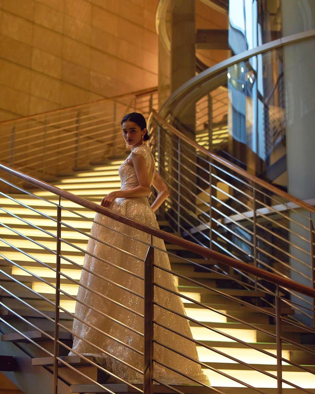 のインスタグラム：「@grandhyatttokyo_wedding のロビーからチャペルへ続く『光の階段』でのショットです。﻿ ﻿ ドレスはシルバーの煌めきが美しい、Galia LahavのGALA-803を着用しています。﻿ ﻿ 華やかでエレガントなハイネックのドレスは、ラグジュアリーなホテルウェディングにぴったりの一着です。﻿ ※ドレスは製作期間として約4~5ヶ月いただいております。﻿ ﻿ dress.﻿ Galia Lahav / GALA-803﻿ ﻿ Handling Salon.﻿ omotesando」