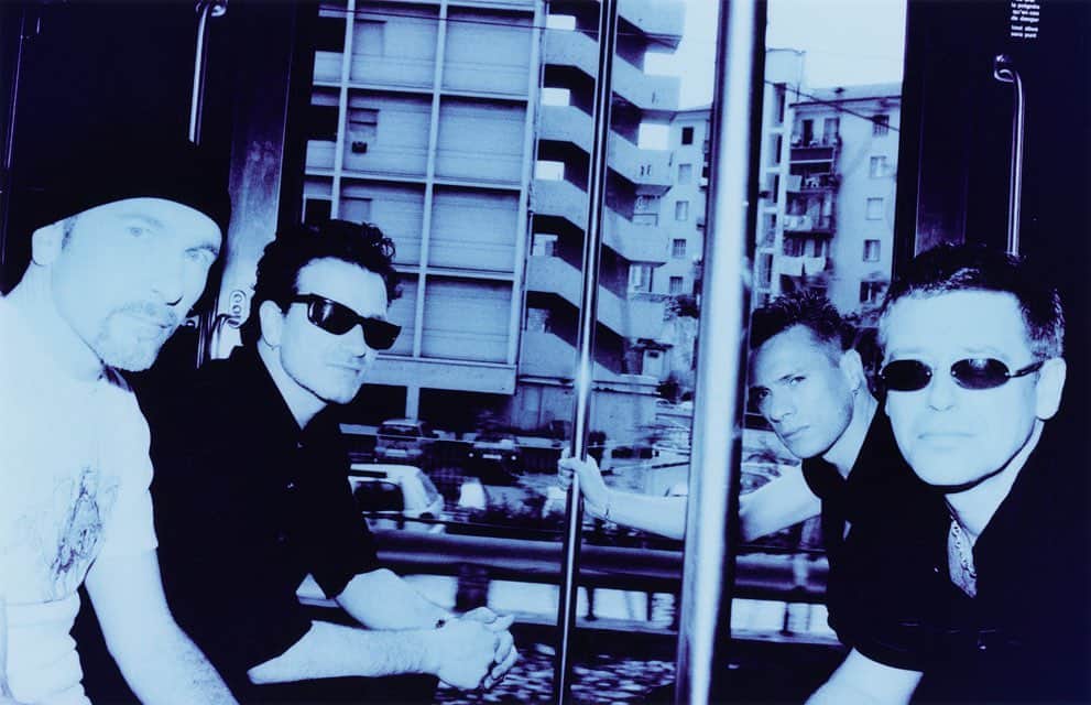 U2さんのインスタグラム写真 - (U2Instagram)「I would be concerned if you still could make this photograph nowadays: riding on a train with the doors open ! But that is how we shot this in 2000 when we took the train from Eze to Nice and shot stuff on the move. And then kind of tried to repeat some of this for the Electrical Storm video in 2002. The slightly chaotic interplay between lines in the foreground and the architecture in the background is utterly random and no 2 frames on my film are the same. The look was created for a project of fake-paparazzi images I was doing late 90’s, shooting on a Polapan (b/w) film with a flash and then printing on colour paper creating a blue with a hint of red to reach a sunshine faded colour look. Like a film poster that has been hanging too long in a closed down cinema in say New Mexico. A conceptual series of images but I loved the look for some work with U2 as well. #AntonU2Takeover @antoncorbijn4real」11月26日 4時01分 - u2