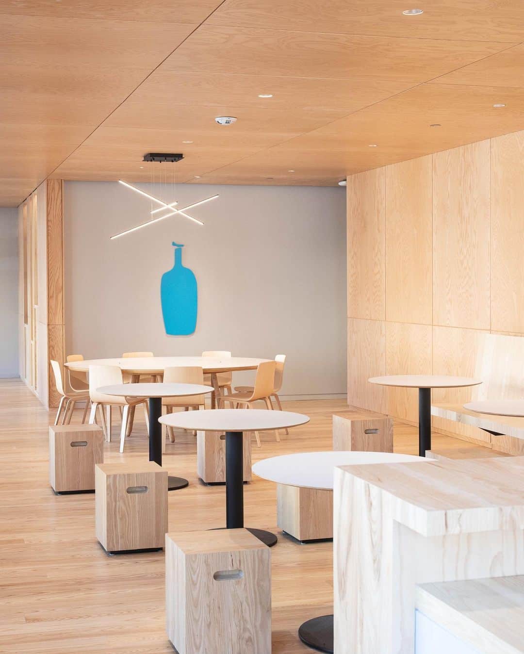 Blue Bottle Coffeeさんのインスタグラム写真 - (Blue Bottle CoffeeInstagram)「Welcome to the Blue Bottle family, B Street!⁠⠀ ⁠⠀ Our B Street cafe resides in a landmark Art Deco building that has been a social hub in San Mateo’s downtown since 1931. Its many incarnations include cigar store, soda fountain, and clandestine hall for bookmakers taking bets. We designed our cafe with such conviviality in mind, conceiving the seating area behind the coffee bar as a “room within a room,” demarcating it with tawny ash wood paneling that clads both ceiling and walls. The effect is like a modernist take on the steak house of yesteryear, where the right mix of darkness and warmth spotlight the immediate pleasures of coffee and food at hand. ⁠⠀ ⁠⠀ In the heart of the seating area is a spacious and round communal table built for Blue Bottle Founder James Freeman. Designed by @bohlincywinskijackson, the same architectural firm that designed this cafe, and built by Tomlinson Woodworks, the table, once used in Freeman's home, is now a space to gather and enjoy our rotating selection of single origins and blends, and our seasonal culinary menu.⁠⠀」12月3日 2時37分 - bluebottle