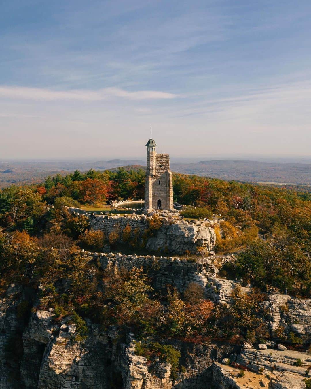 National Geographic Travelさんのインスタグラム写真 - (National Geographic TravelInstagram)「Photo and video by @MichaelGeorge / The rocky ridges of the Shawangunk Mountains look like a giant slammed his foot down on the floorboards of the Earth, jutting a piece of bedrock into the air. The ridges rise above the surrounding farmland and fall trees, creating a spectacular contrast of gray and black against the red and orange tree cover. If you’re staying at the Mohonk Mountain House, a short hike to the Skytop Tower will give you one of the best views of the area. If you’re not staying there, you can get a day pass to hike the four miles round trip from the Mohonk Gatehouse up to the tower and small reservoir. The tower itself is a memorial to Albert K. Smiley, who co-founded the Mountain House with his twin brother, Alfred. In the video (swipe to view), you’ll see the reservoir that was created from the quarry where they took the rock for the tower. The leftover rock can be seen lining the carriage roads that lead up to the tower. The Skytop Tower is an icon of the Shawangunk skyline and can be seen all the way from the nearby town of New Paltz, New York.  For more photos and writing from my travels, follow along @MichaelGeorge. #skytoptower #mohonkmountainhouse #newpaltz #shawangunkmountains #thegunks」12月5日 0時39分 - natgeotravel