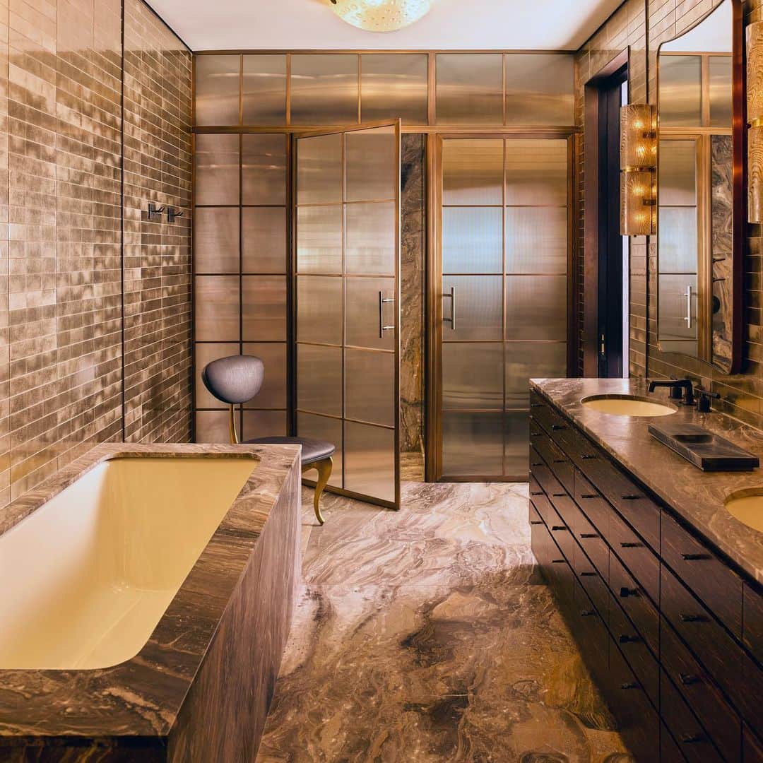 ケリーウェアスラーのインスタグラム：「RAW & REFINED. This master bath is an ode to natural materials in their most glamorous incarnation. Patinated brass divided light doors frame ribbed glass, walls are clad in luminescent glass tiles, and vintage smoke glass sconces illuminate the space. XK」