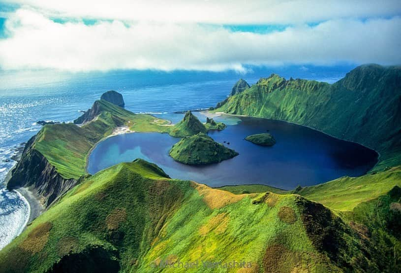 Michael Yamashitaさんのインスタグラム写真 - (Michael YamashitaInstagram)「Yankicha Island - The summertime mist that cloaks this remote island, part of the Kuril island chain, imparts a mystical quality. Billed as one of the least visited places on the planet, Yankicha sees only the occasional cruise ship that stops there. I flew over the island in a Russian helicopter but had no permission to land. Caught between Russia and Japan, surrounded by the Pacific Ocean and the Sea of Okhotsk, tiny Yankicha is a volcanic island located in the center of the Kuril archipelago that’s just 1.25 miles (2 kilometers) in diameter. The islet is the top of a partially submerged still-active volcano, which last erupted in 1884, with two small lava domes forming small islands in a central lagoon. Numerous fumaroles and hot springs edge the southeast caldera shoreline. It has no human residents but it abounds with wildlife, including Arctic foxes, seals, and rare birds. It's actually the southern half of a larger island, Ushishir, whose name is derived from the Ainu language for "hot spring".  The Ainu people, the original inhabitants of the Kurils, were an indigenous tribe with roots in both Russia and Japan. They considered Yankicha a sacred place and used it for shamanic rituals. The islands were later settled by the Japanese, followed by the Russians. #yankicha kurilislands #kuril #ainu #volcano #volcanicisland」12月7日 2時56分 - yamashitaphoto