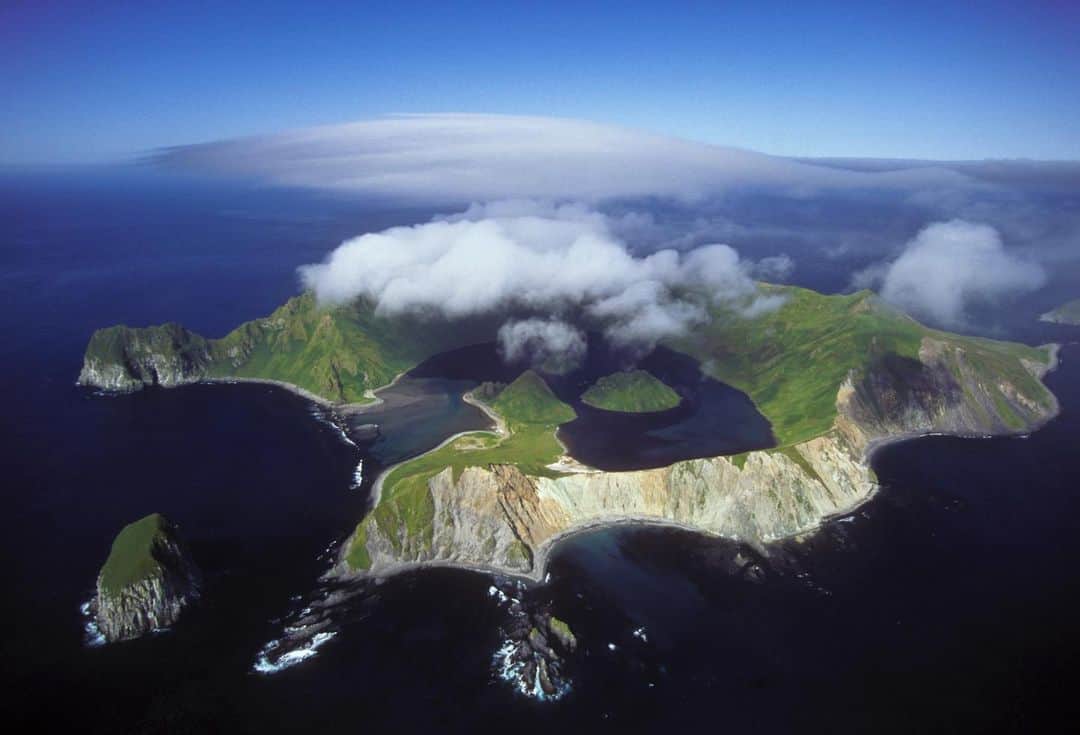 のインスタグラム：「Yankicha Island - The summertime mist that cloaks this remote island, part of the Kuril island chain, imparts a mystical quality. Billed as one of the least visited places on the planet, Yankicha sees only the occasional cruise ship that stops there. I flew over the island in a Russian helicopter but had no permission to land. Caught between Russia and Japan, surrounded by the Pacific Ocean and the Sea of Okhotsk, tiny Yankicha is a volcanic island located in the center of the Kuril archipelago that’s just 1.25 miles (2 kilometers) in diameter. The islet is the top of a partially submerged still-active volcano, which last erupted in 1884, with two small lava domes forming small islands in a central lagoon. Numerous fumaroles and hot springs edge the southeast caldera shoreline. It has no human residents but it abounds with wildlife, including Arctic foxes, seals, and rare birds. It's actually the southern half of a larger island, Ushishir, whose name is derived from the Ainu language for "hot spring".  The Ainu people, the original inhabitants of the Kurils, were an indigenous tribe with roots in both Russia and Japan. They considered Yankicha a sacred place and used it for shamanic rituals. The islands were later settled by the Japanese, followed by the Russians. #yankicha kurilislands #kuril #ainu #volcano #volcanicisland」