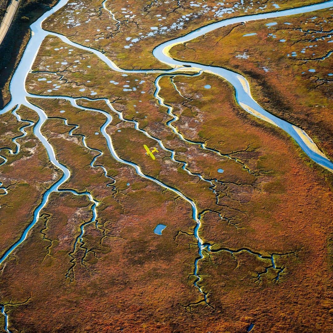 クリス・バーカードのインスタグラム：「A seemingly uninteresting estuary comes alive at low tide. Crisp morning light illuminates its veins. A small yellow biplane cuts across the sky while 1,000 ft above I peek out of the small window of a Cessna 210 shooting with a 24-70 mm lens.  This image was taken near my home during the filming of a new Aerial workshop. I wanted more than anything to demonstrate that without proper planning, vision & patience for the perfect weather- you simply cannot buy your way into a good photograph. I have shot this landscape many times over many years and each time learned a little bit more about its subtleties, it’s secrets. These are the images to me that mean the most, the ones that force us to look at a familiar scene with new eyes.」